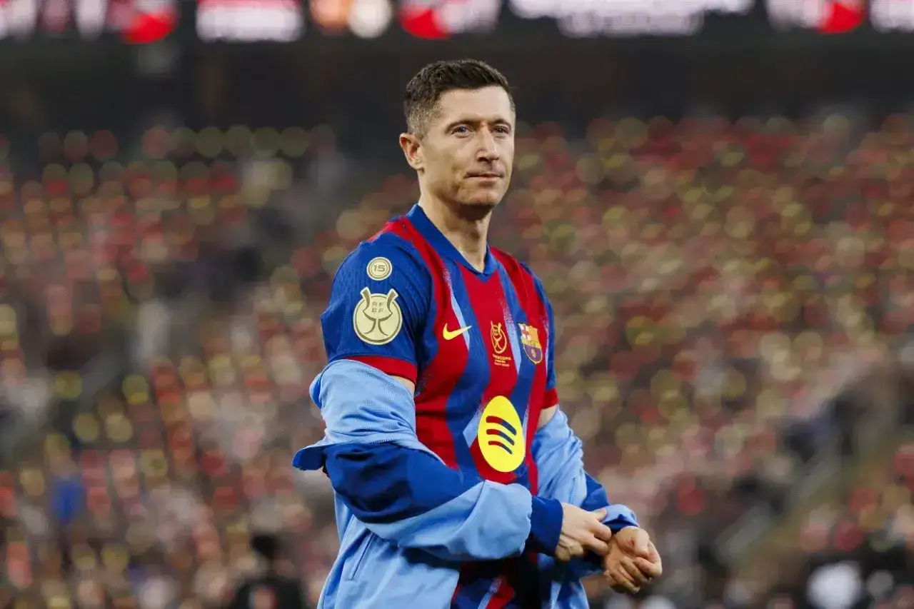 Robert Lewandowski w koszulce Barcelony, symbol jego wysokich zarobków piłkarzy. Tło to rozmyte trybuny stadionu.