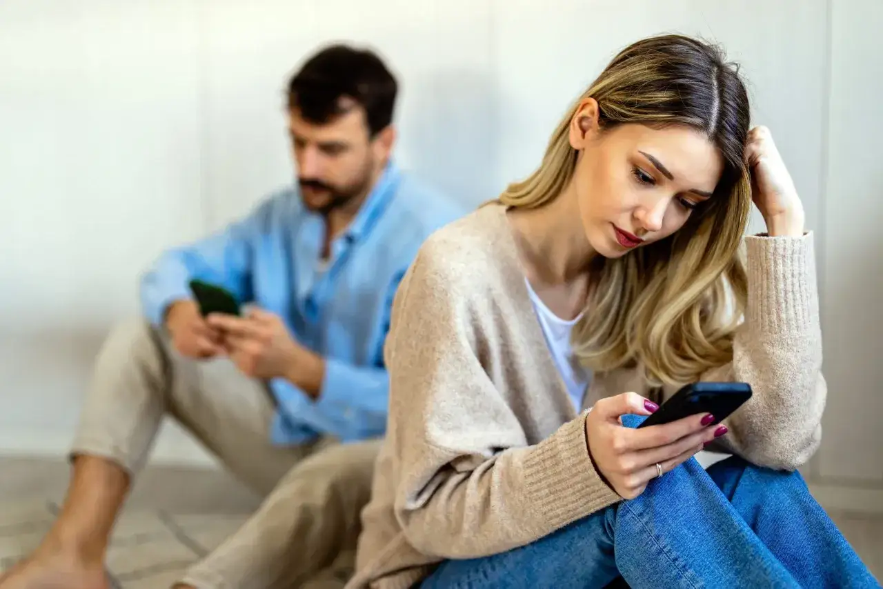 Een vrouw en man zitten apart, beiden op hun telefoon. Ze voelen zich eenzaam, ik mis liefde in mijn relatie.