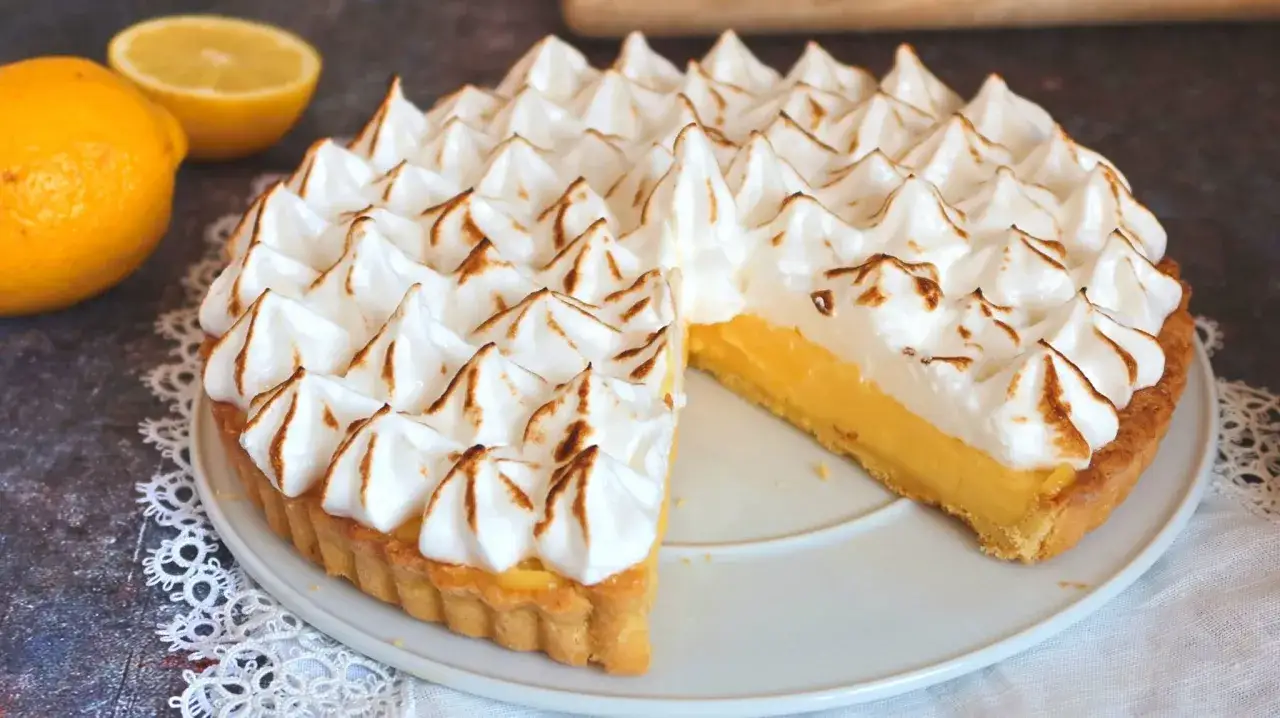 Un delicioso lemon pie con merengue dorado y una porción cortada, junto a limones frescos.