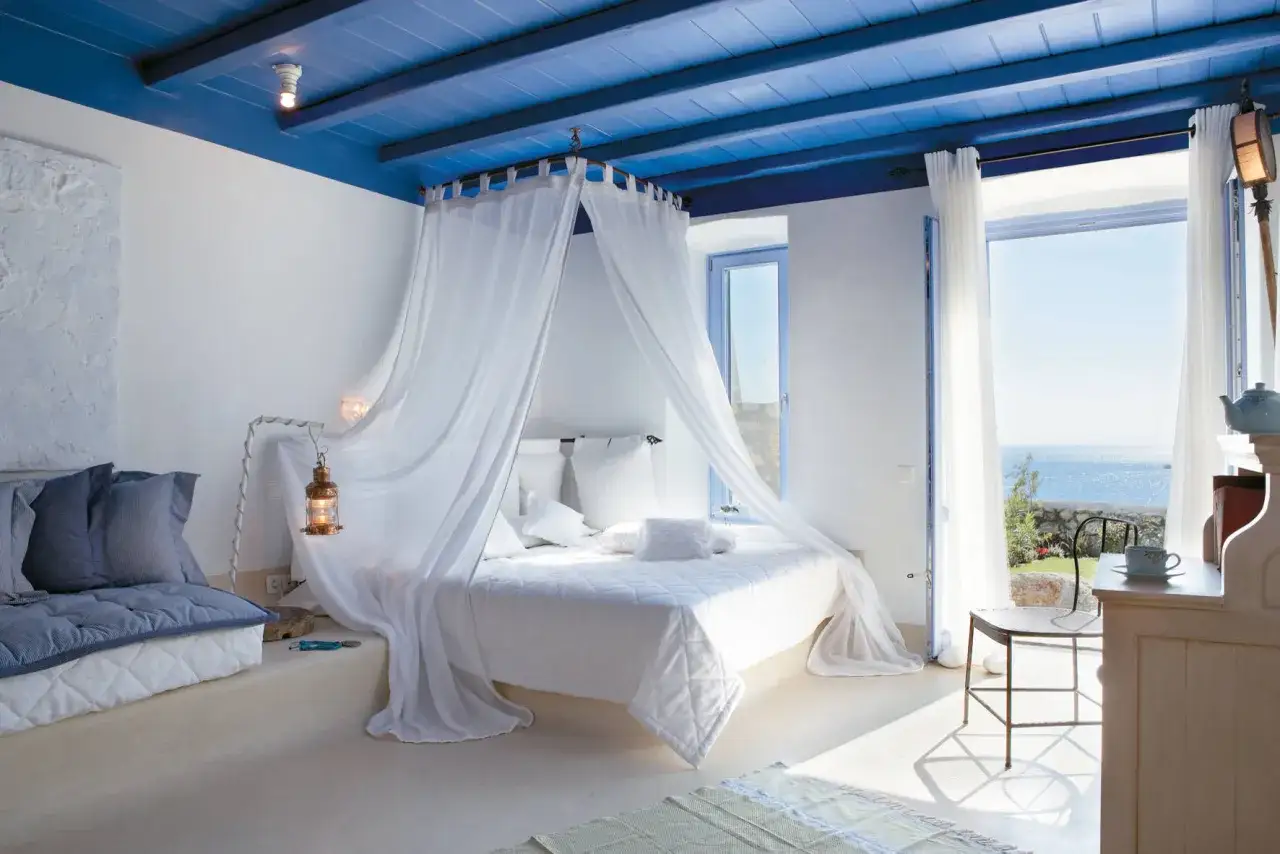 Camera da letto casa al mare con soffitto blu, letto a baldacchino bianco e vista sull'oceano.