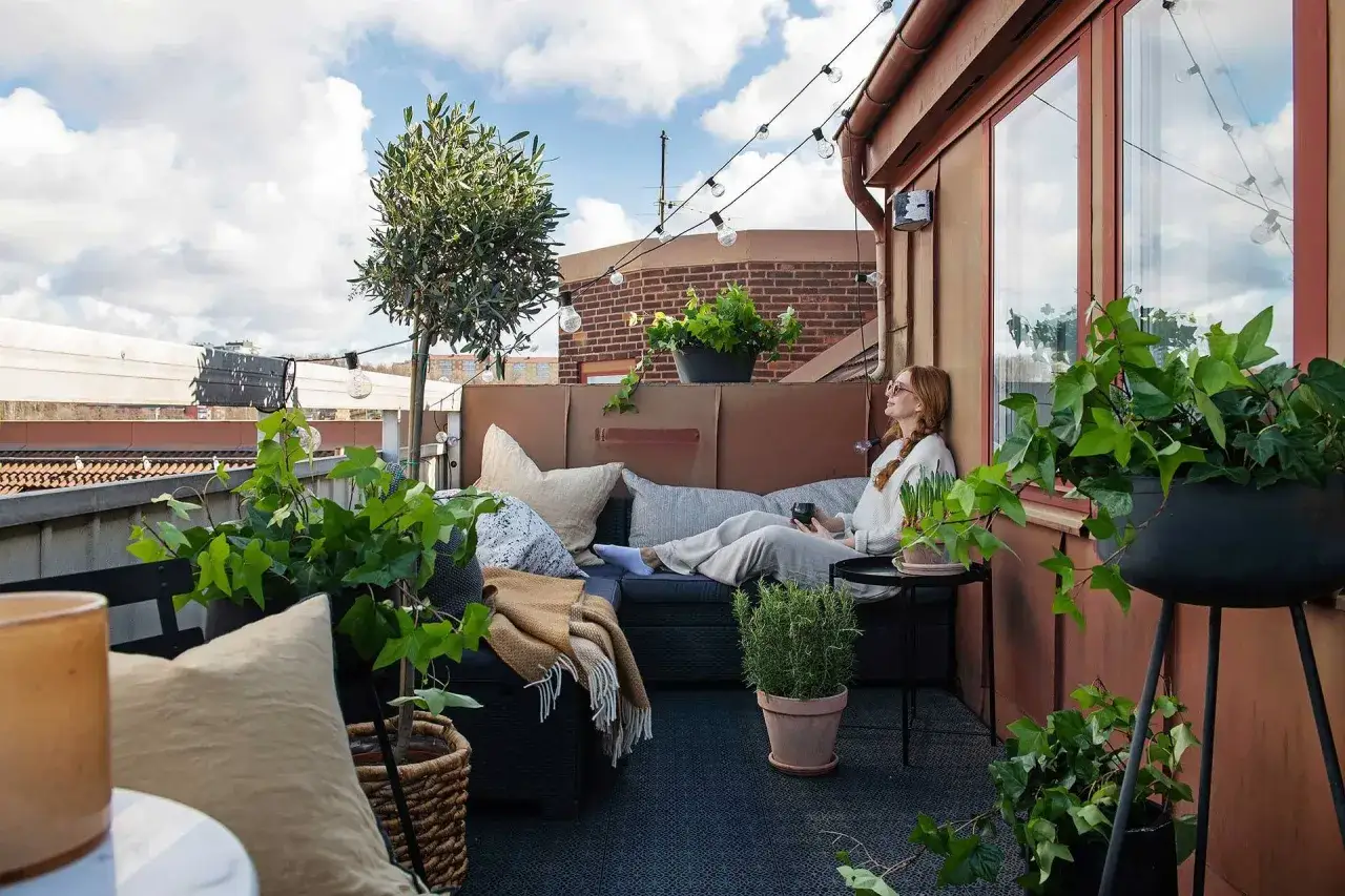Mujer relajada en un balc&oacute;n alargado decorado con plantas y luces.