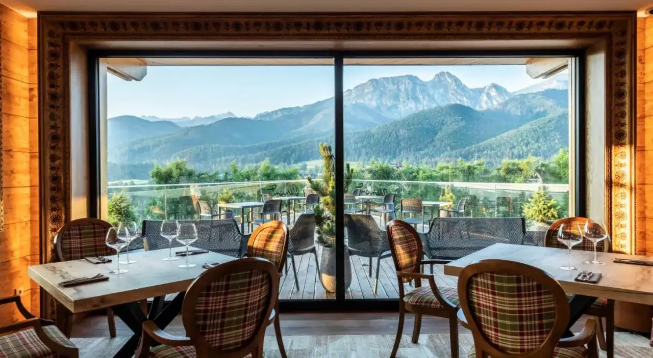 Elegancka restauracja z gwiazdką Michelin, z widokiem na góry. Stoły nakryte, gotowe na przyjęcie gości.