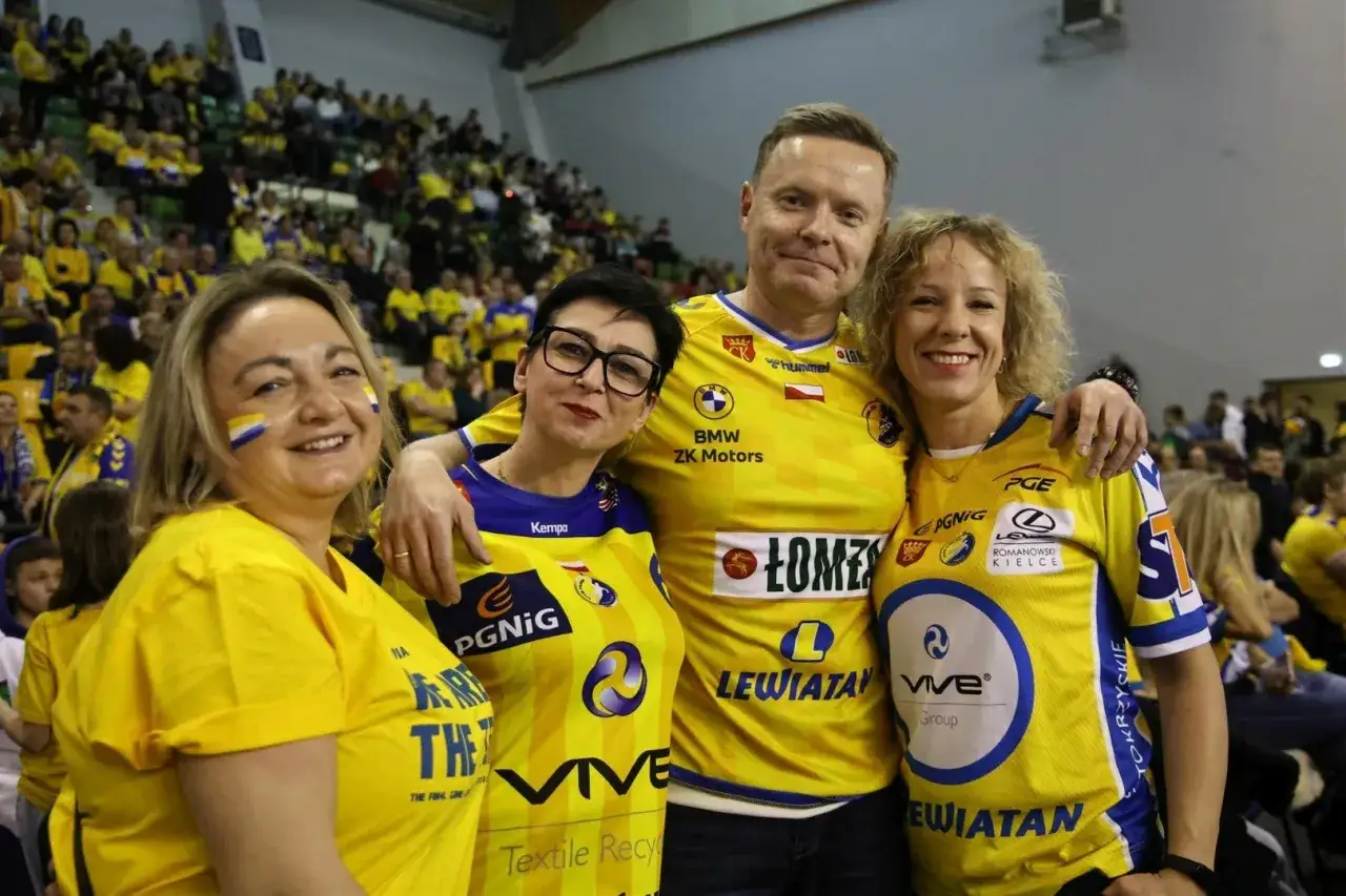 Uśmiechnięci kibice w ż&oacute;łtych koszulkach z logo VIVE Kielce, wspierający swoją drużynę na meczu.