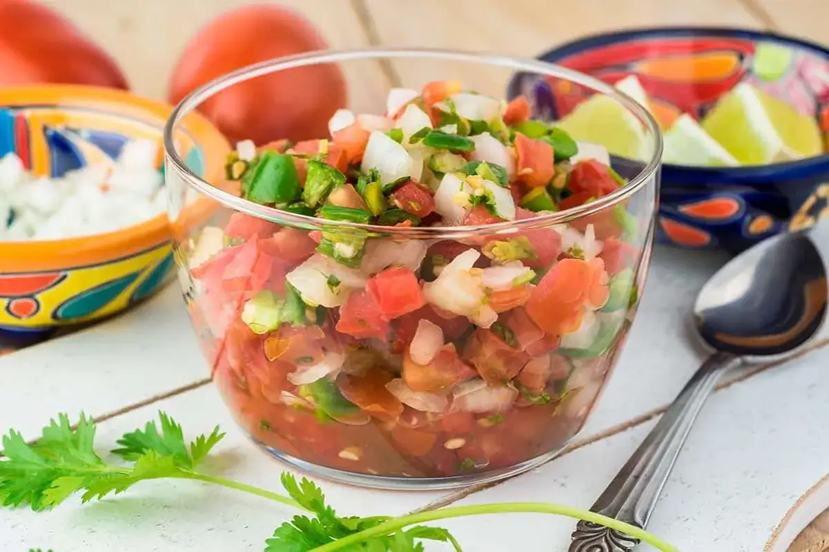 Un taz&oacute;n de **salsa criolla** fresca, con tomate, cebolla y chile verde picados. Acompa&ntilde;ada de cilantro y limones.