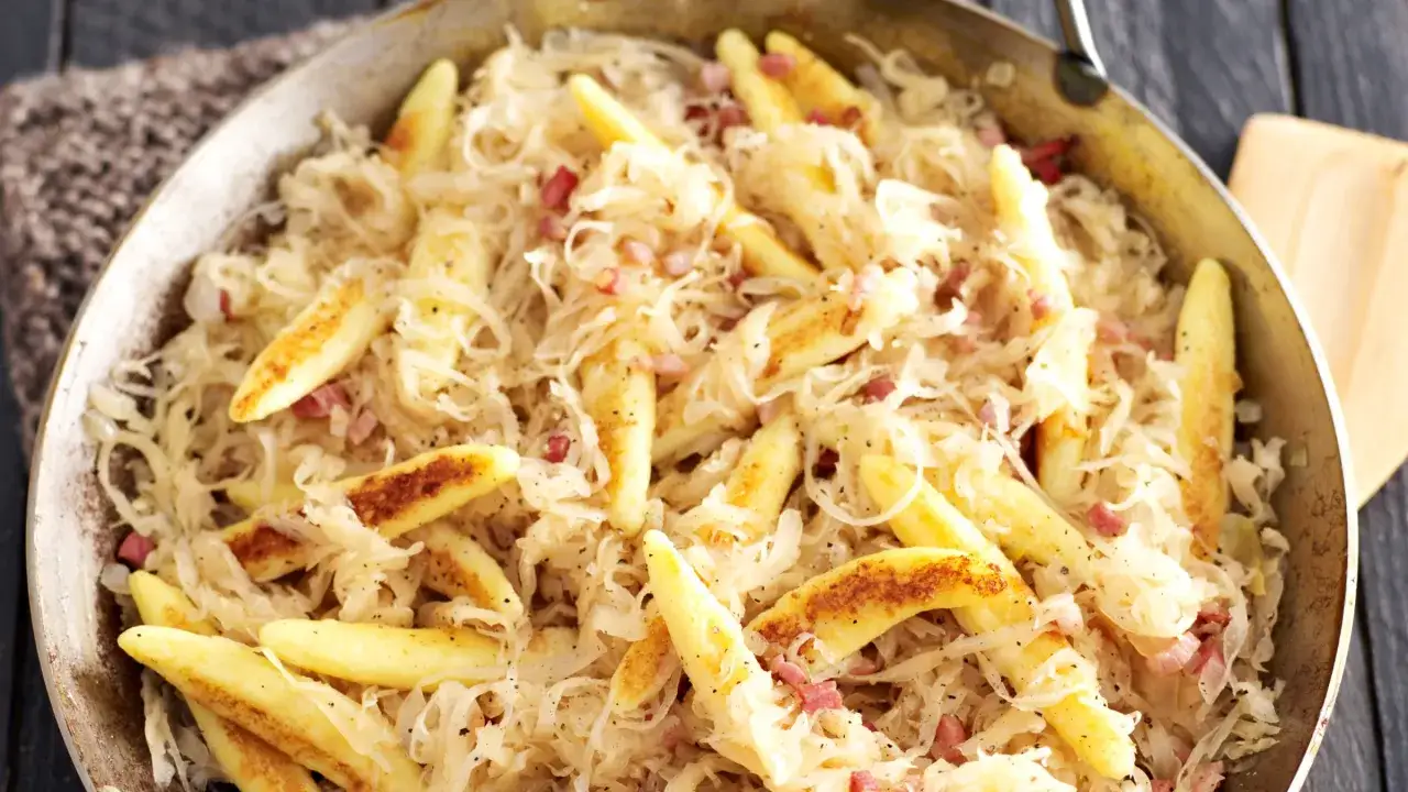 Schupfnudeln mit Sauerkraut und Speckwürfeln in einer Pfanne. Ein herzhaftes Gericht, das zum Genießen einlädt.