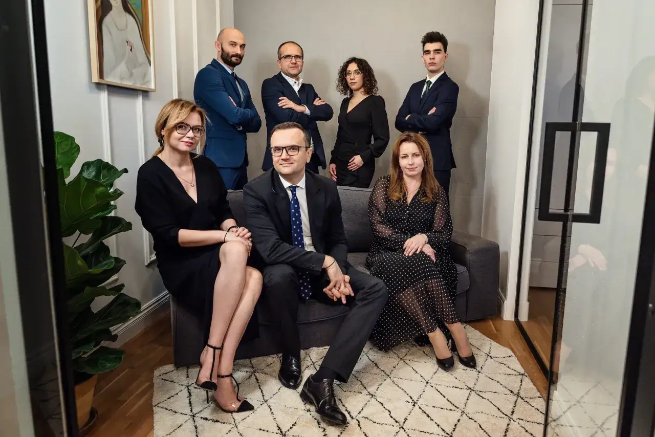 Grupa prawników i adwokatów w eleganckich strojach pozuje w nowoczesnym wnętrzu.