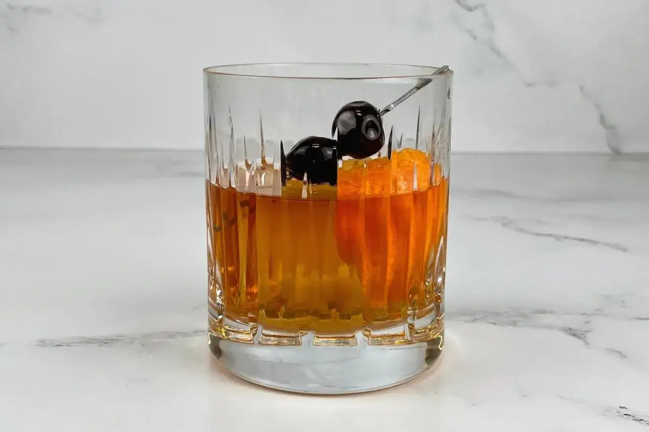 En old fashioned-drink med apelsinskal och körsbär i ett glas med räfflor.