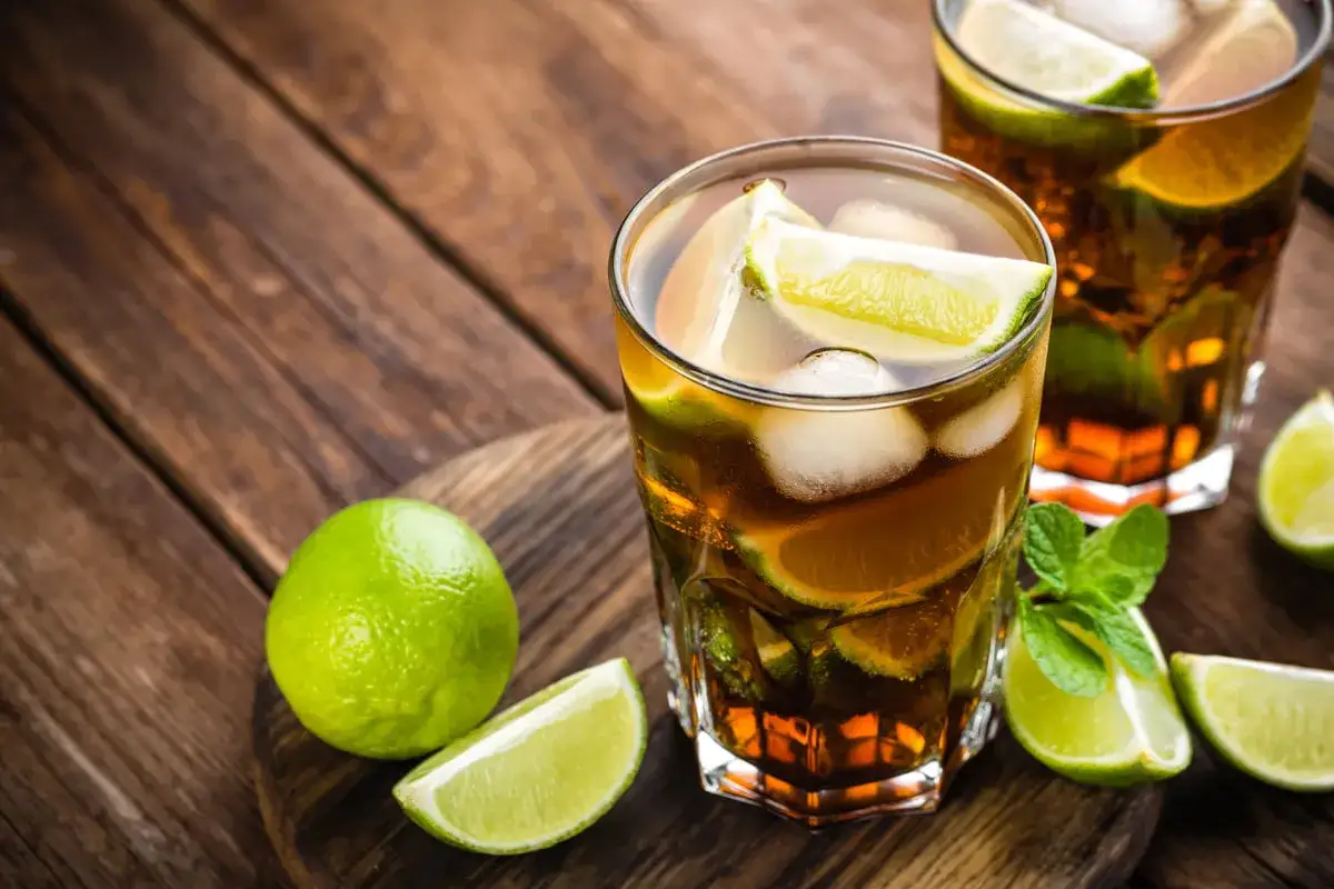 Tv&aring; glas med rom och cola, is och lime. En hel lime och n&aring;gra limeklyftor ligger bredvid.