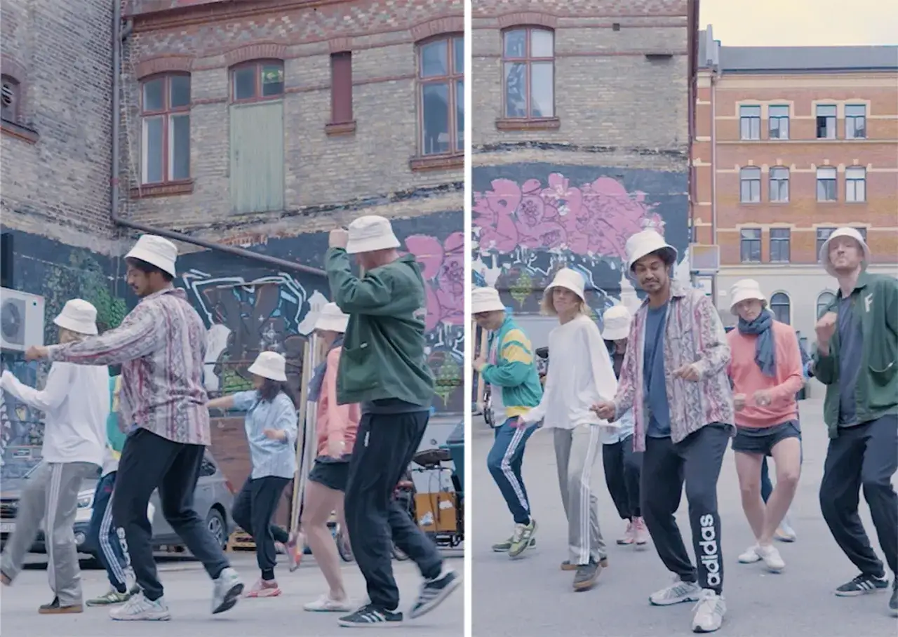 En grupp m&auml;nniskor med hinkhattar dansar i en gr&auml;nd i Stockholm. De r&ouml;r sig synkroniserat till musiken, med en positiv och energisk atmosf&auml;r.