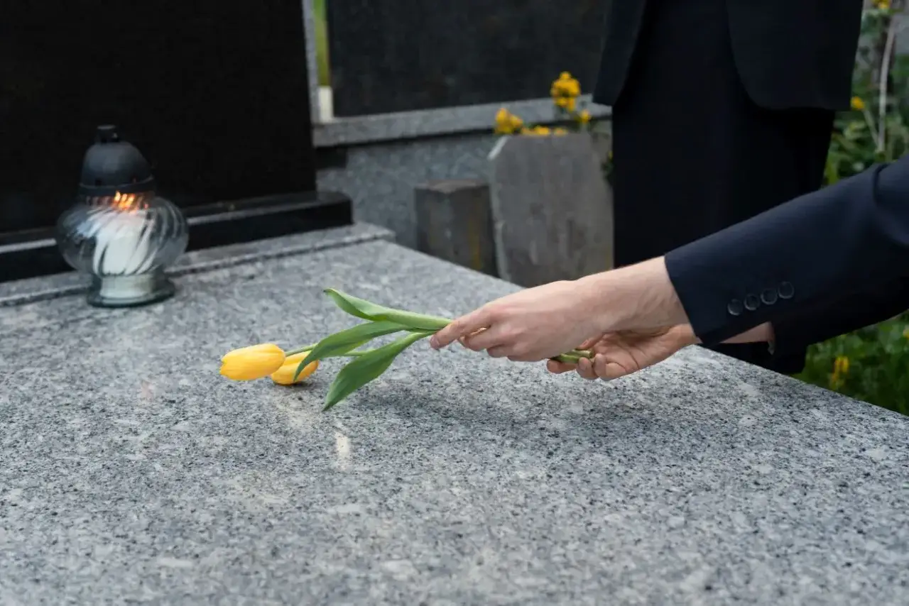 Dłoń kładzie żółte tulipany na granitowym nagrobku obok palącej się znicza. Jak zabezpieczyć pomnik z granitu?