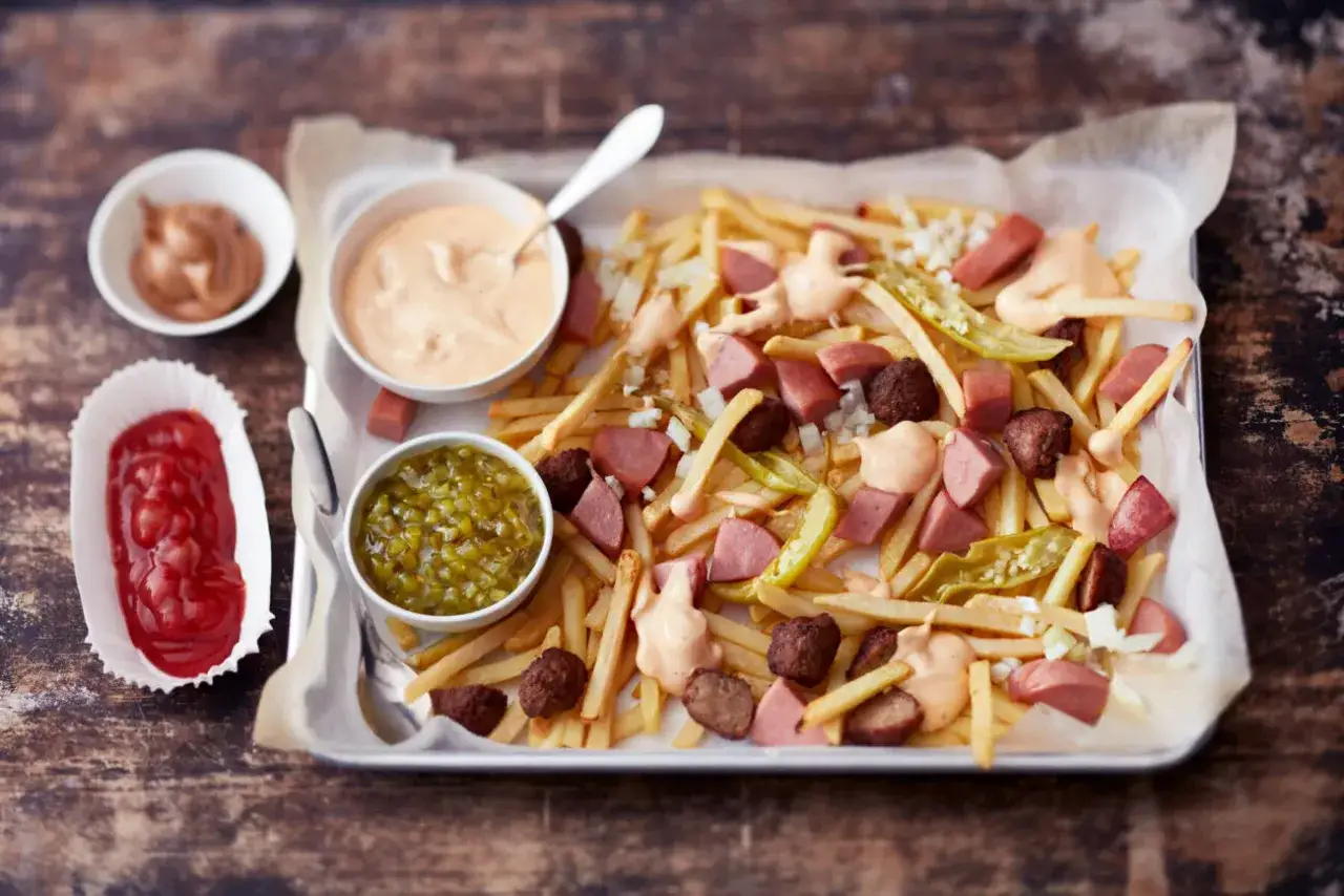 Pommes frites med korv, k&ouml;ttbullar och en kr&auml;mig s&aring;s till pommes. Serveras med ketchup och inlagd gurka.