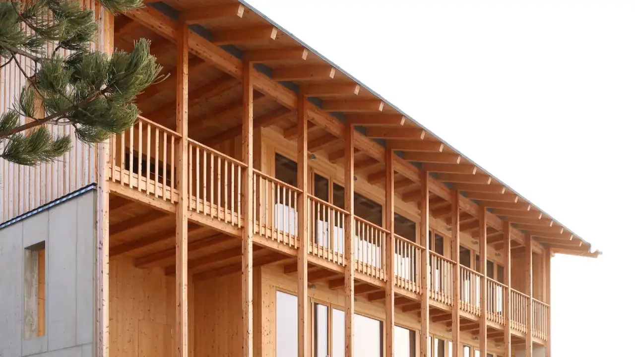 Ein modernes Frame Haus aus Holz mit Balkonen und gro&szlig;en Fenstern. Ein Baum ragt ins Bild.