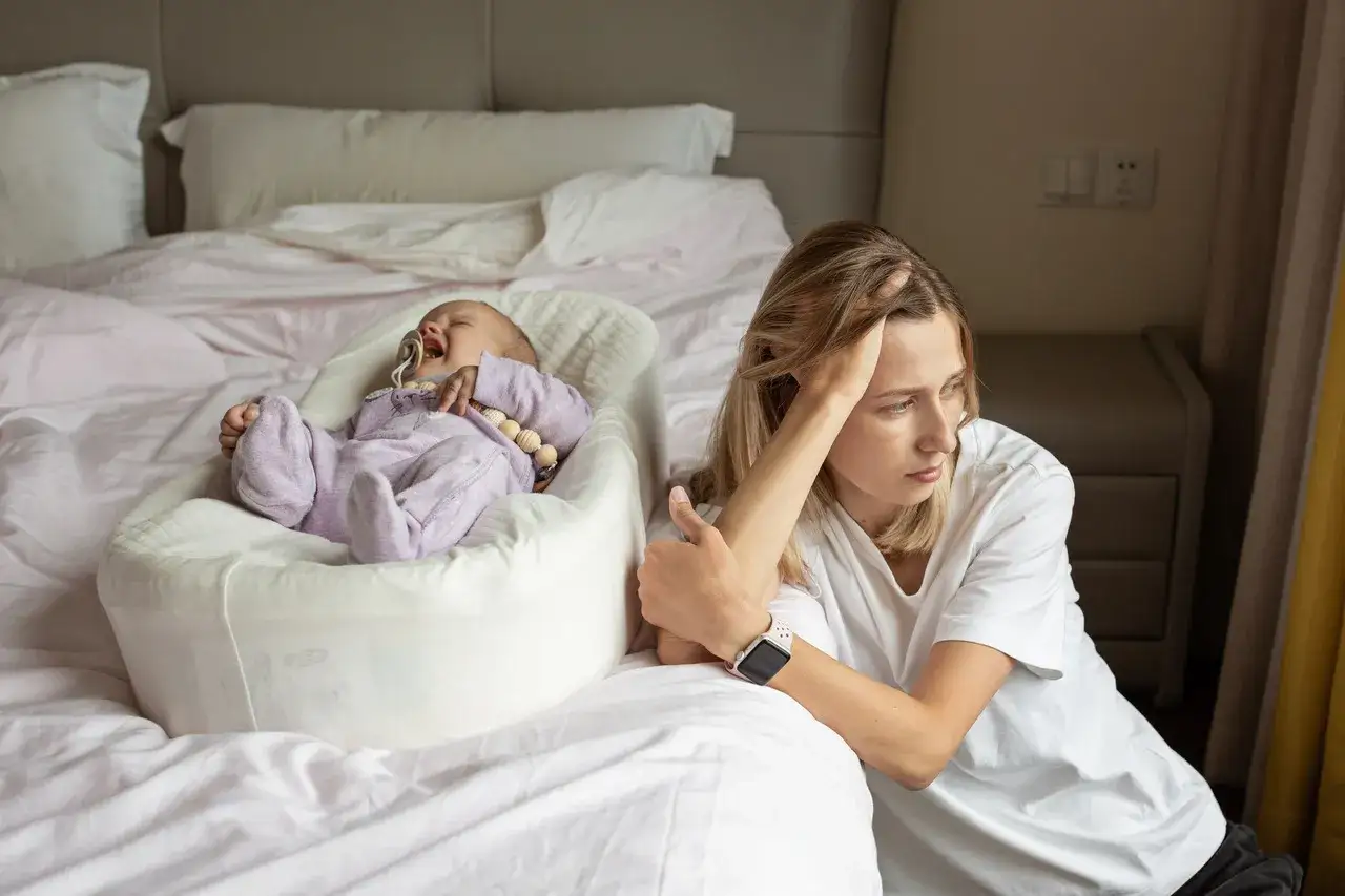 Zmęczona mama patrzy na płaczące dziecko. Czasem opieka nad maleństwem to prawdziwe wyzwanie dla **baby brain**.