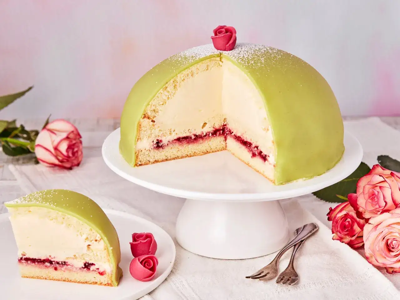 Ein Anschnitt eines grünen Prinzessinnenkuchens mit Sahnefüllung und Himbeermarmelade, verziert mit einer Zuckerrose.