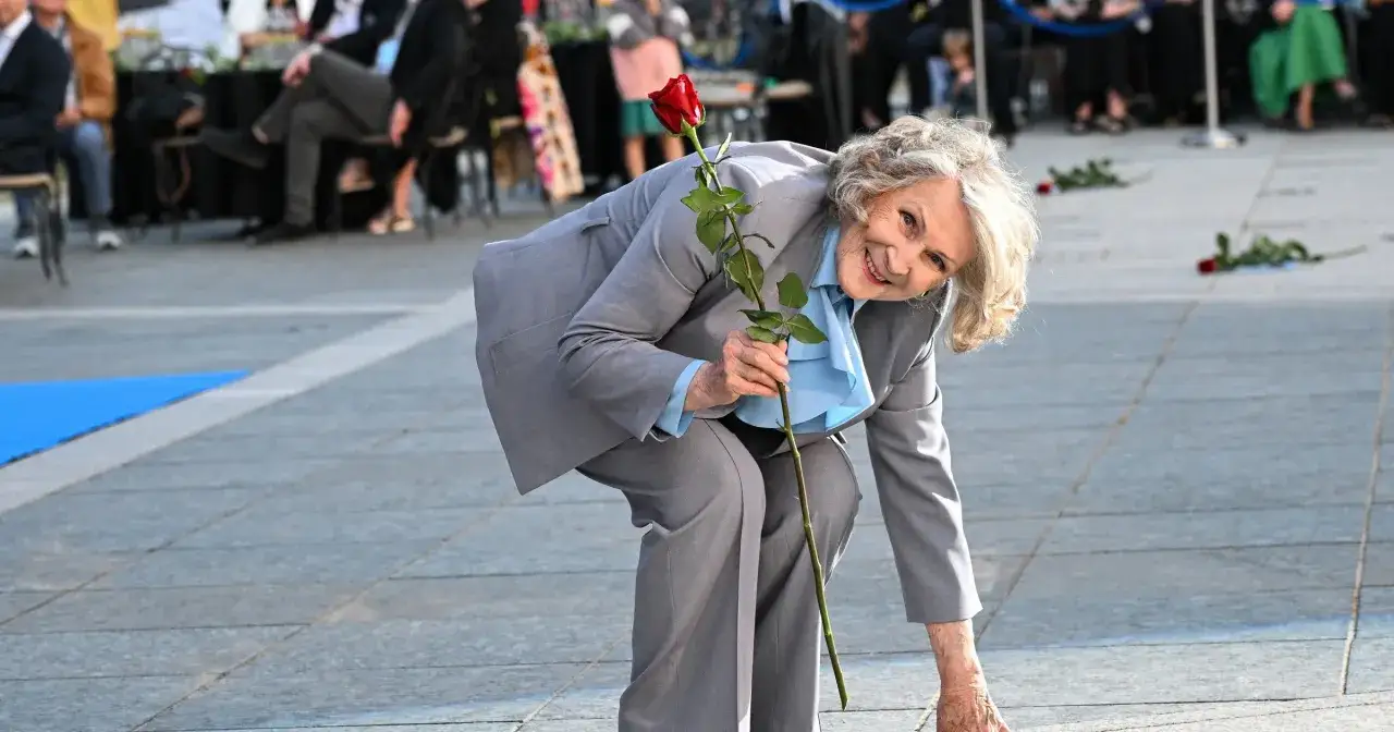 Uśmiechnięta Irena Santor, choć już nie żyje, kładzie czerwoną różę na bruku.