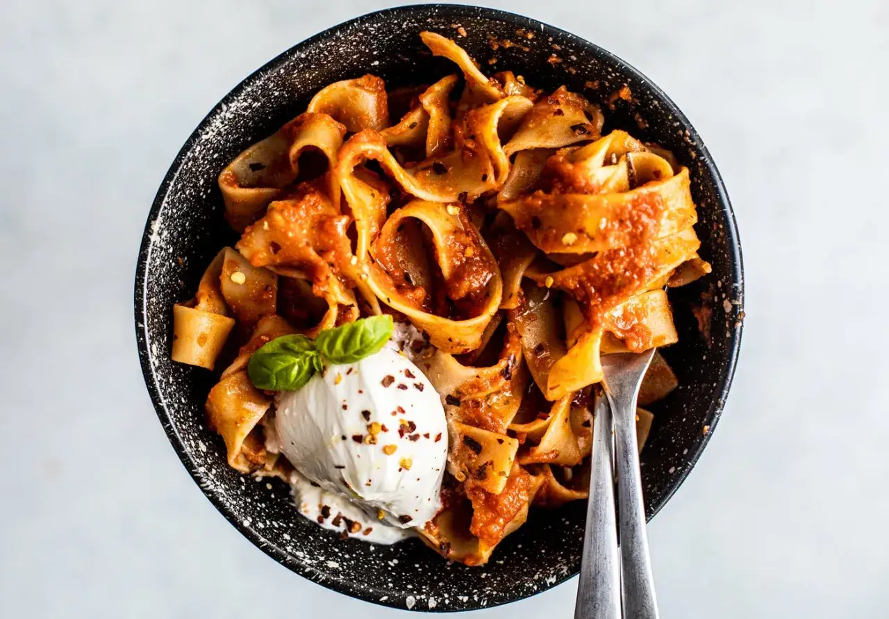 Pappardelle all'arrabbiata z burratą i bazylią, podane w czarnej misce. Pikantny sos pomidorowy idealnie komponuje się z kremowym serem.