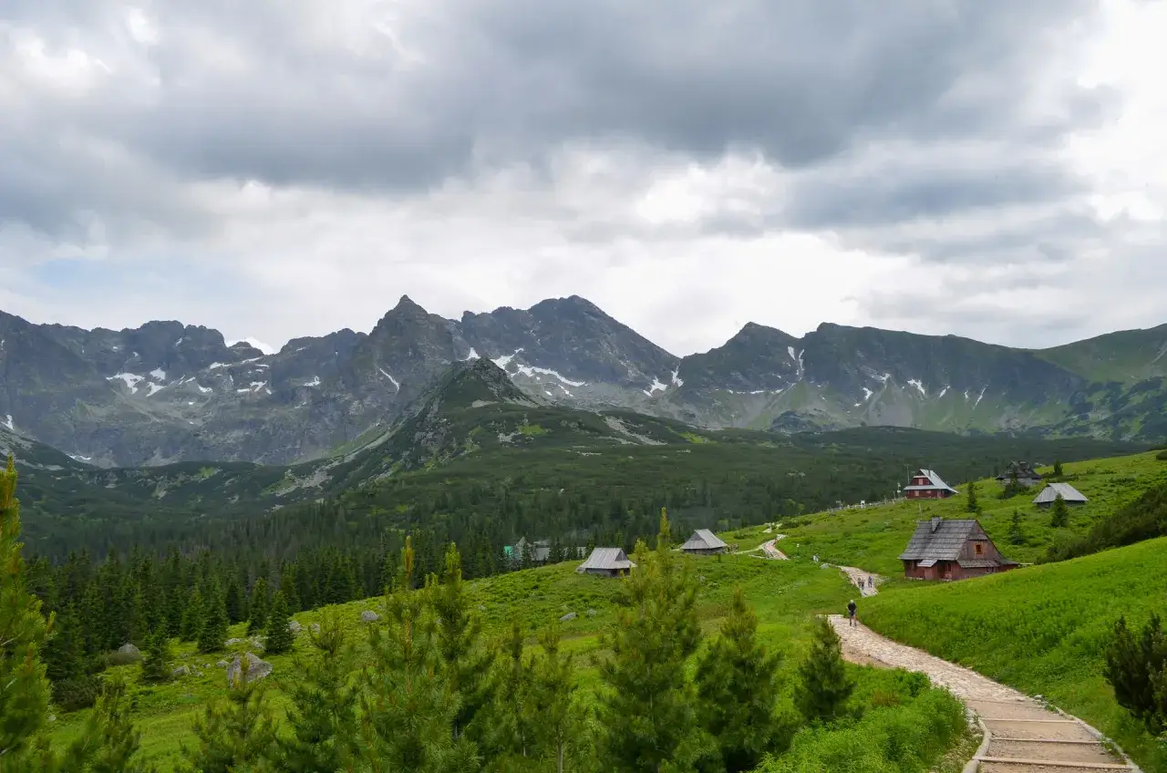 Widok na Tatry z zielonymi zboczami i kilkoma drewnianymi chatkami. Szlak z brzezin do murowańca zamknięty, ale widok zapiera dech.