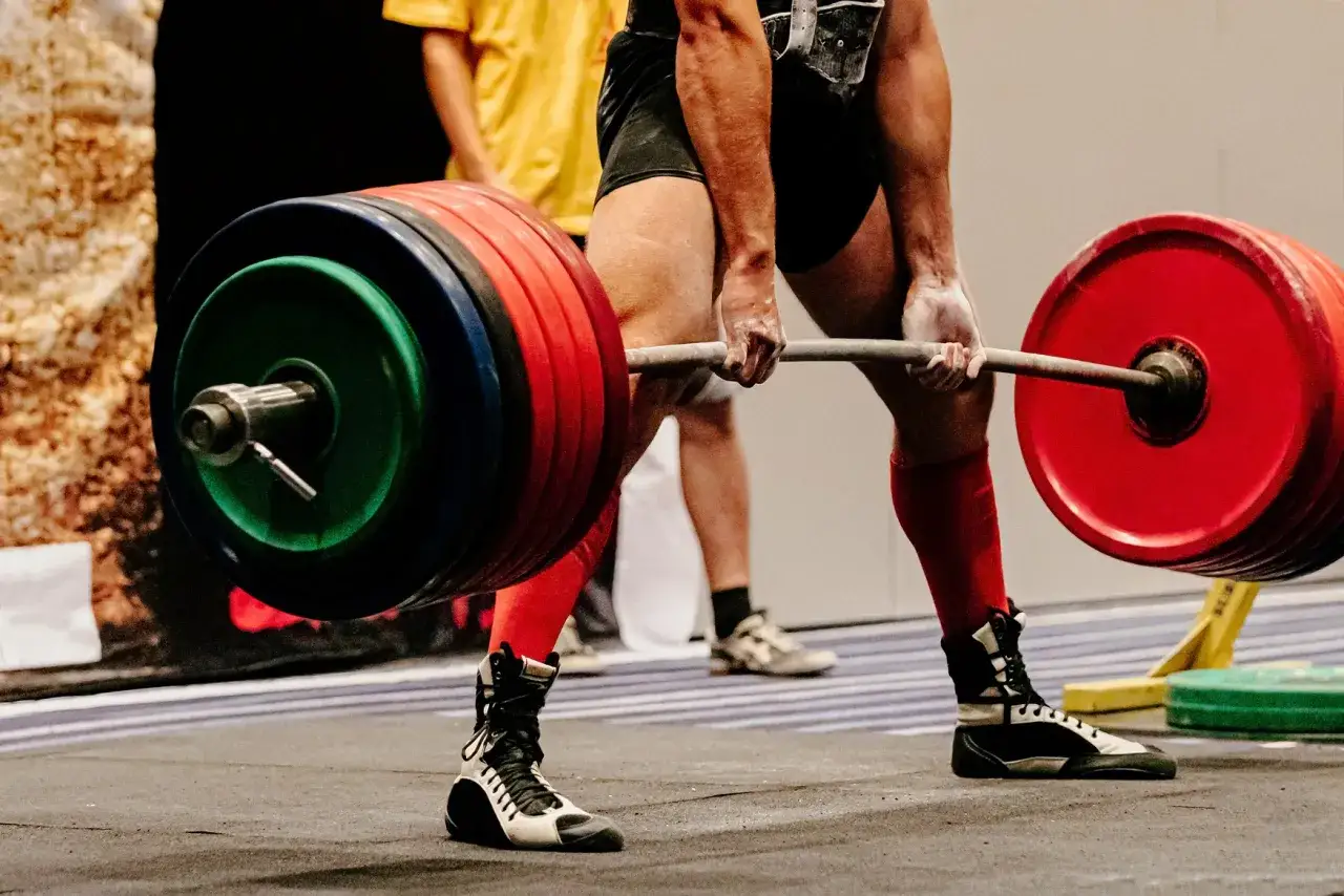 Atleta in pieno allenamento powerlifting, solleva un bilanciere carico di pesi colorati. Gambe potenti e concentrazione massima.