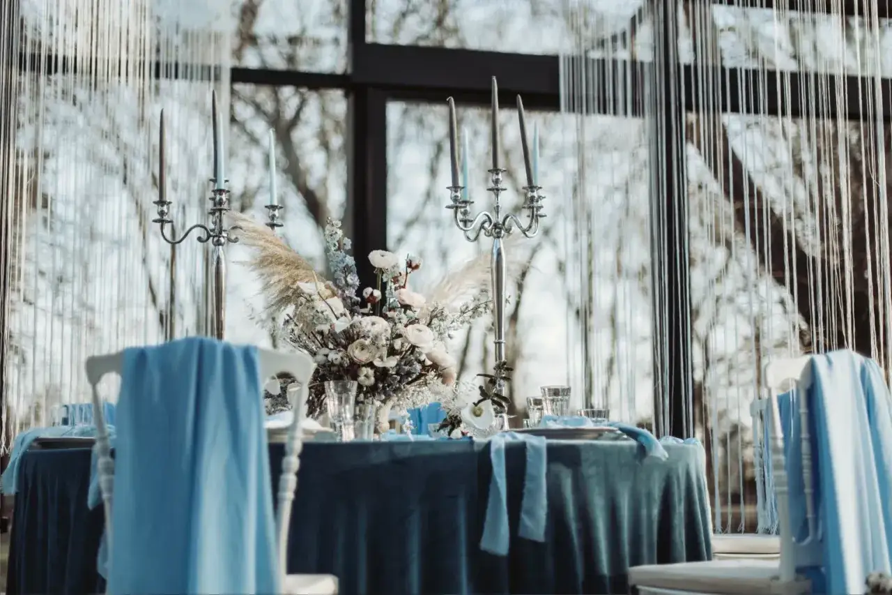 Eleganckie wesele w grudniu. St&oacute;ł nakryty błękitnym obrusem, ozdobiony świecznikami i bukietem z traw pampasowych.