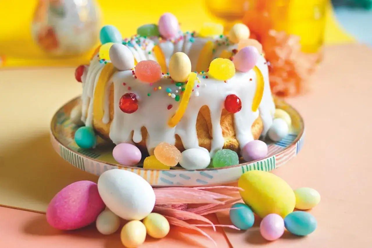 Dolci pasquali decorati con glassa bianca, caramelle colorate e confetti a forma di uovo, pronti per essere gustati.