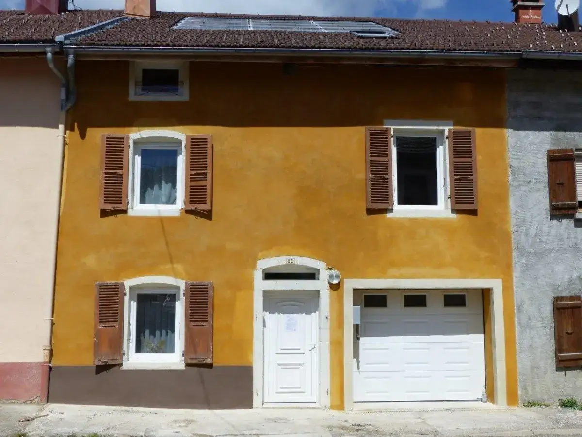 Façade ocre d'une maison avec volets en bois marron. La chaux morte a été appliquée sur le mur, lui donnant une texture unique.