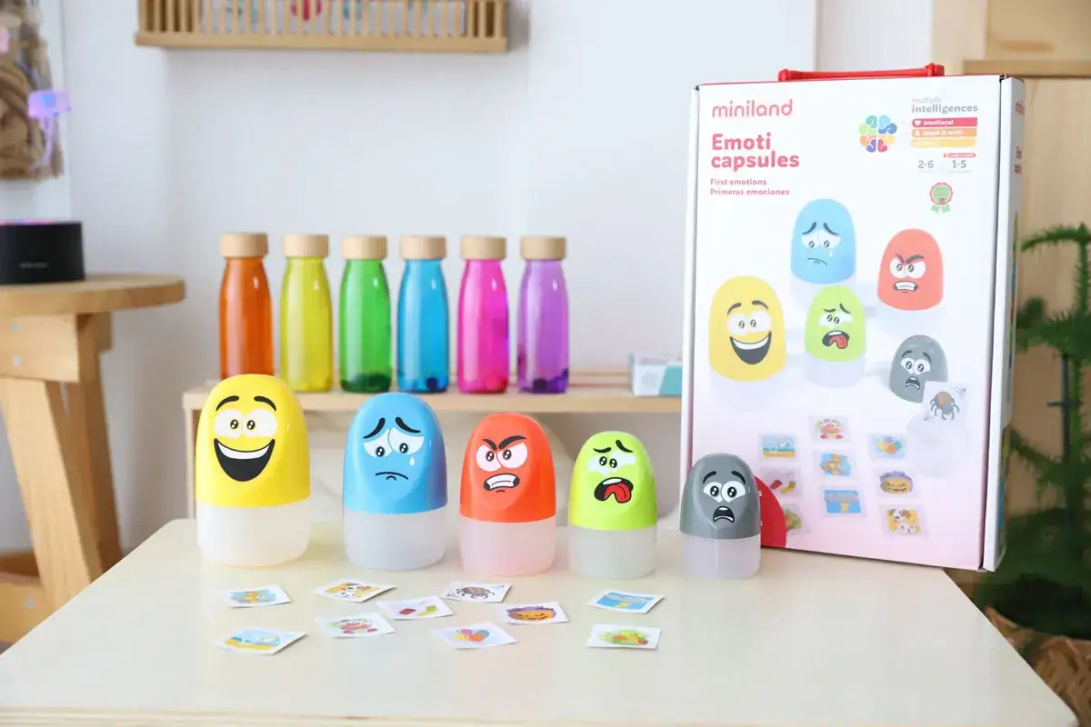 Juguetes para la inteligencia emocional de niños: cápsulas con caras de emociones y tarjetas ilustradas.
