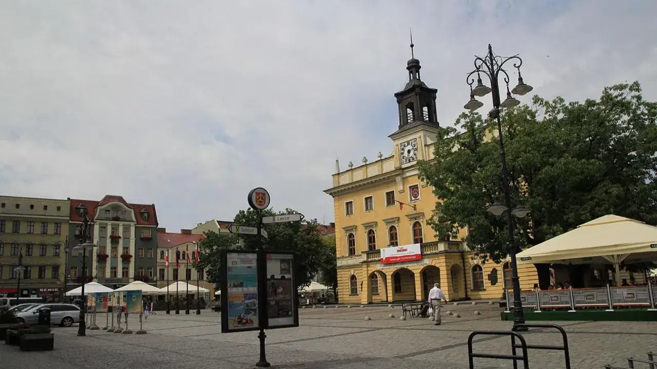 Rynek w wielkopolskim mieście koło Kalisza. Ż&oacute;łty ratusz z wieżą, kolorowe kamienice, kawiarniany ogr&oacute;dek i brukowany plac.
