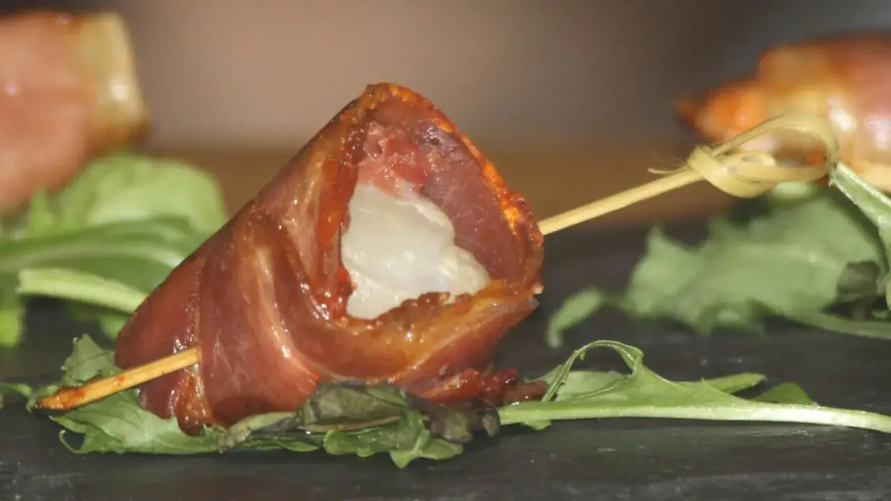 Brochette de noix de Saint-Jacques enroul&eacute;e de lard, cuite &agrave; la plancha, servie sur un lit de verdure.