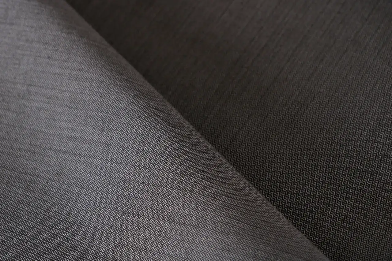 Tessuto twill grigio scuro con trama a spina di pesce, ideale per abbigliamento invernale o estivo.