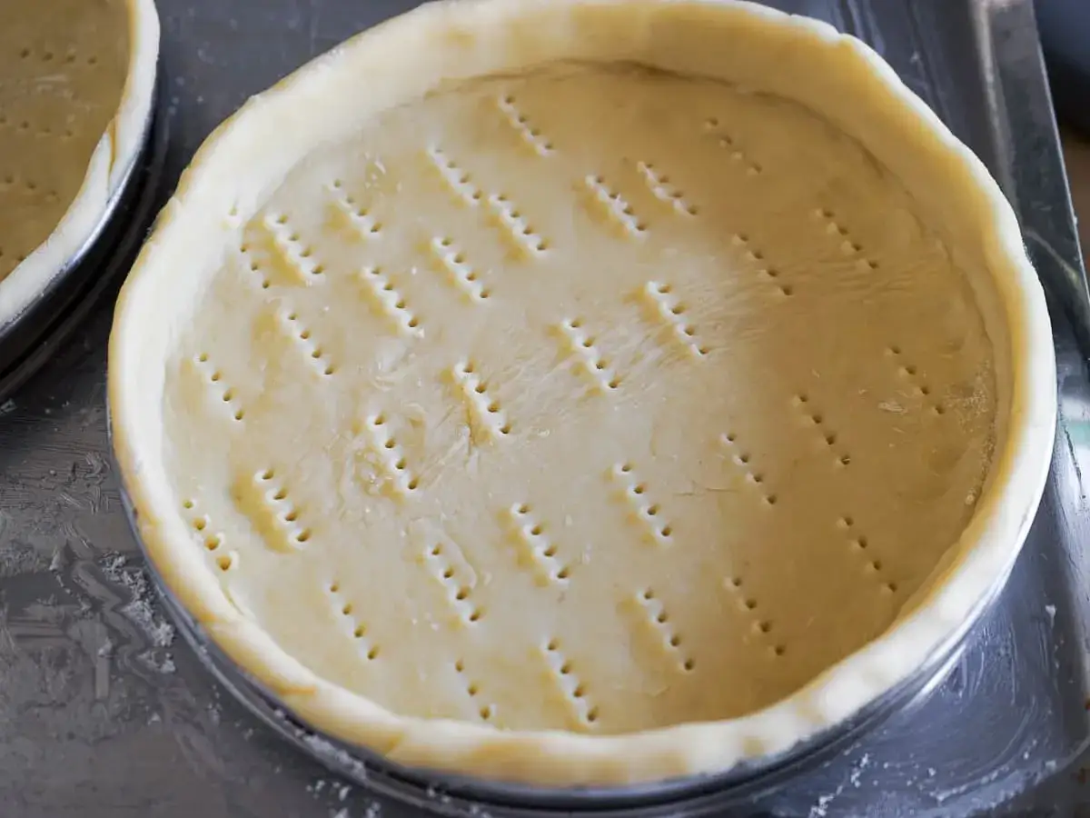 Pâte brisée prête pour la cuisson, piquée de trous pour une dorure parfaite.