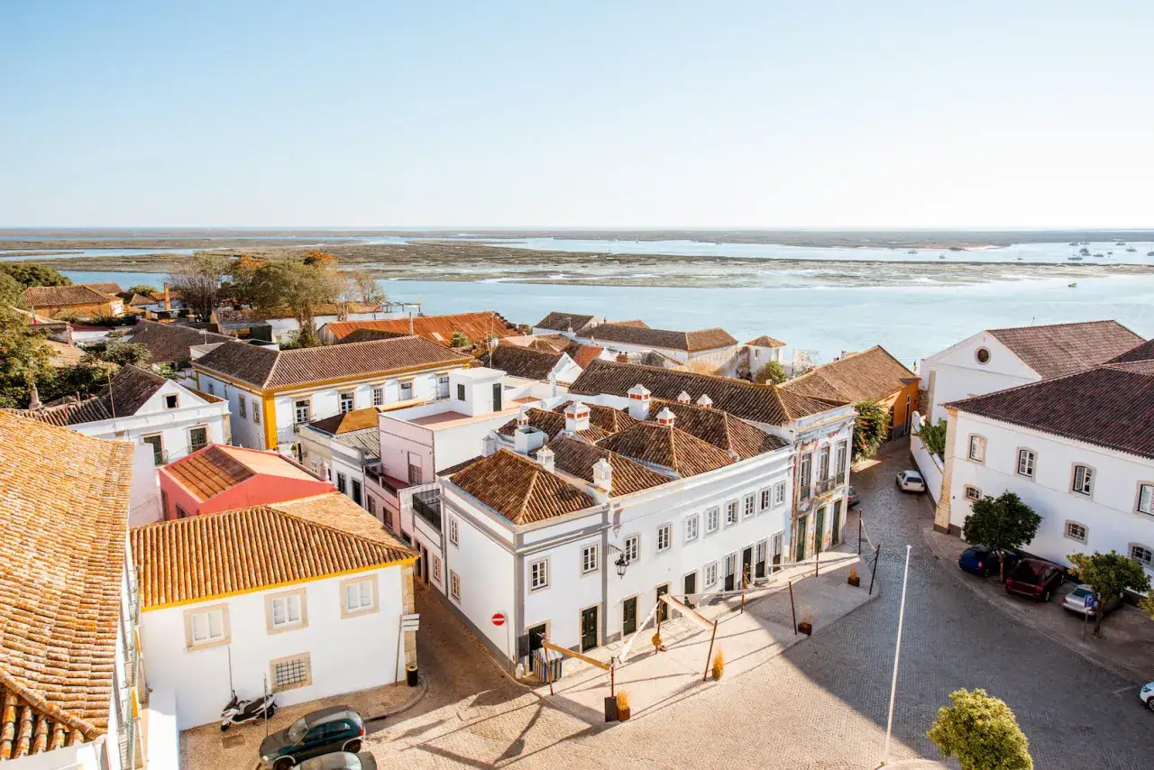 D&auml;cher und wei&szlig;e H&auml;user im distrikt Faro, mit Blick auf das ruhige Wasser und Boote am Horizont.