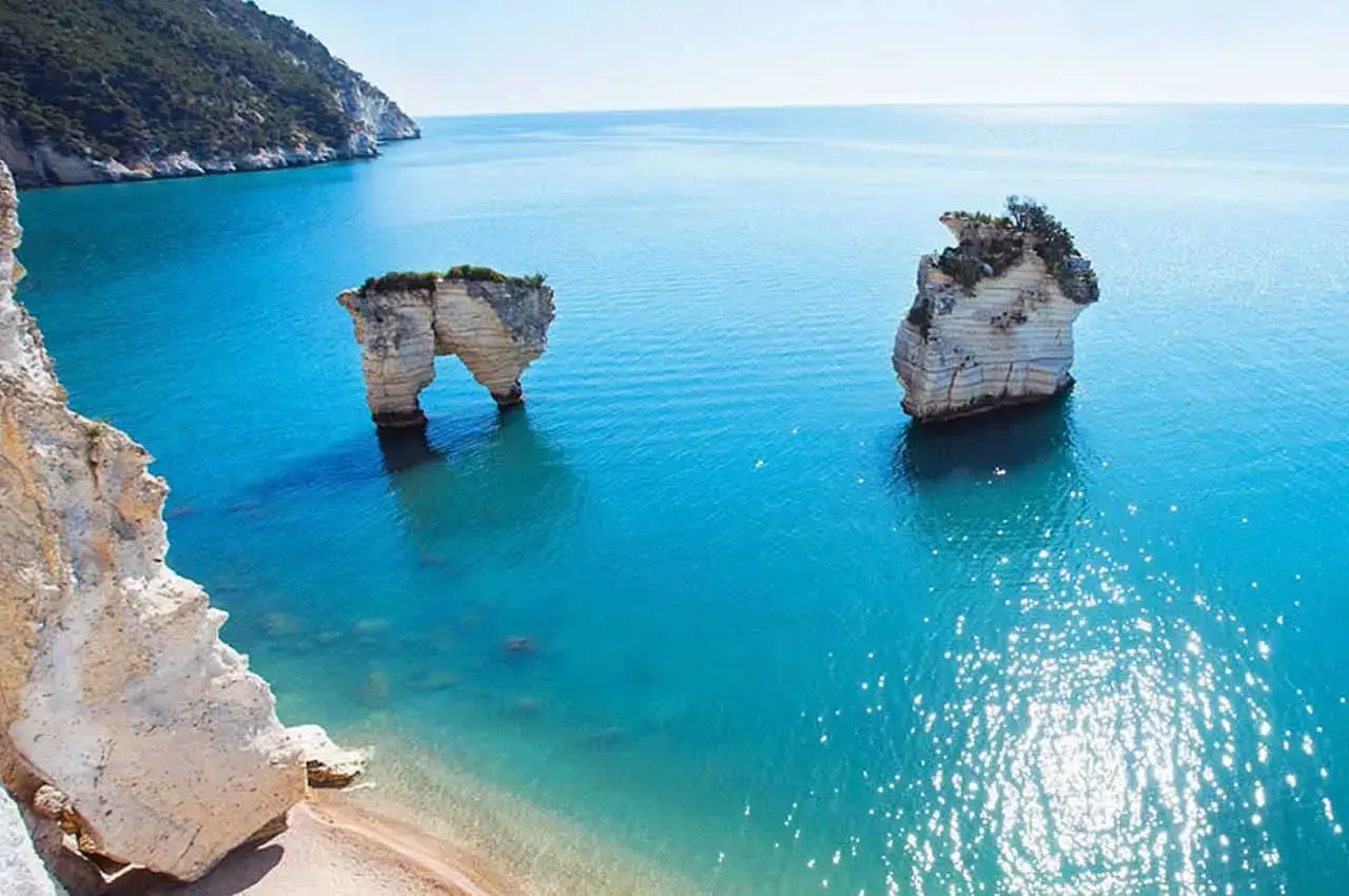 Faraglioni di roccia bianca emergono dal mare cristallino di Rodi, Puglia. Un arco naturale scolpito dal vento e dal mare.