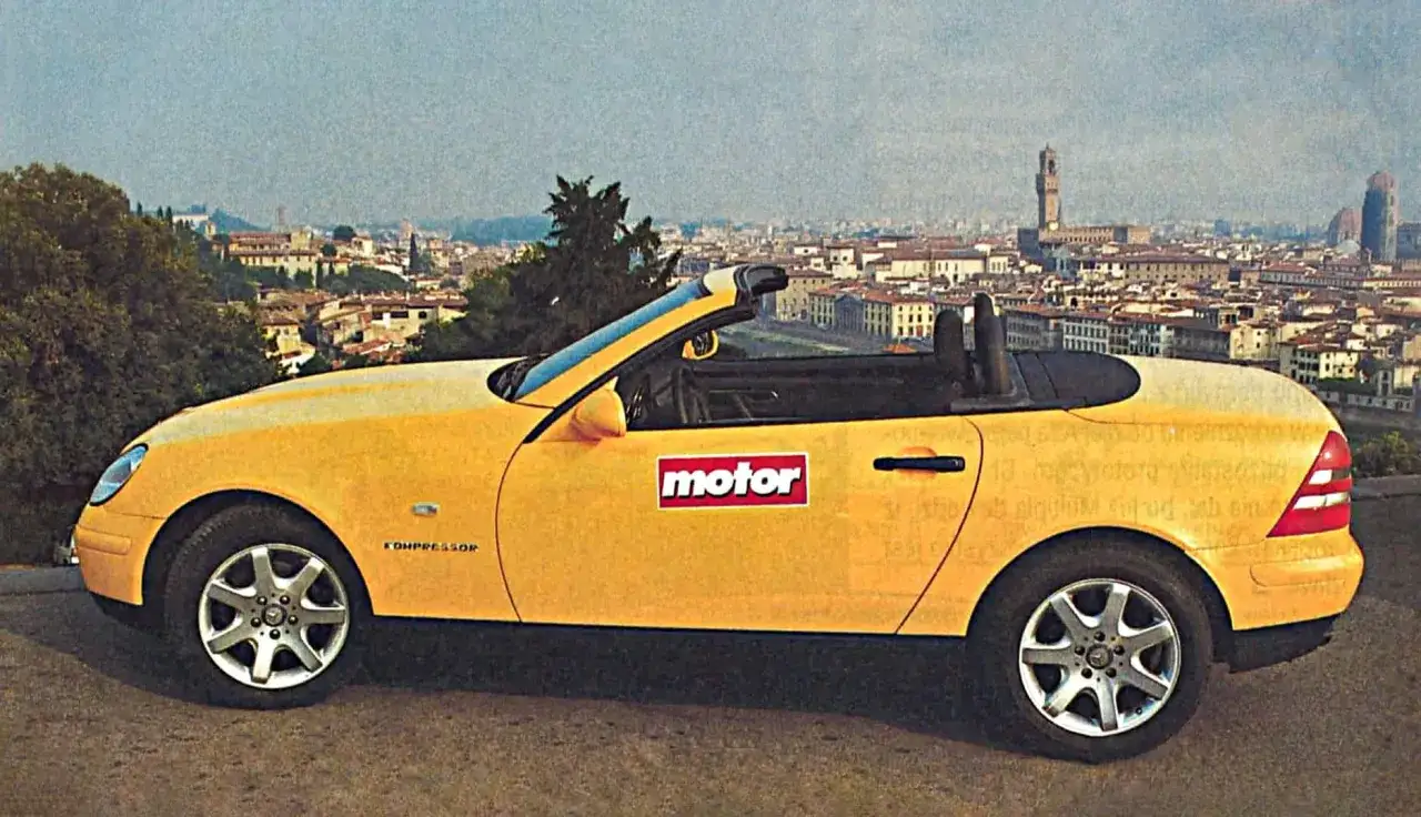 Żółty Mercedes SLK 200 z otwartym dachem na tle panoramy miasta.