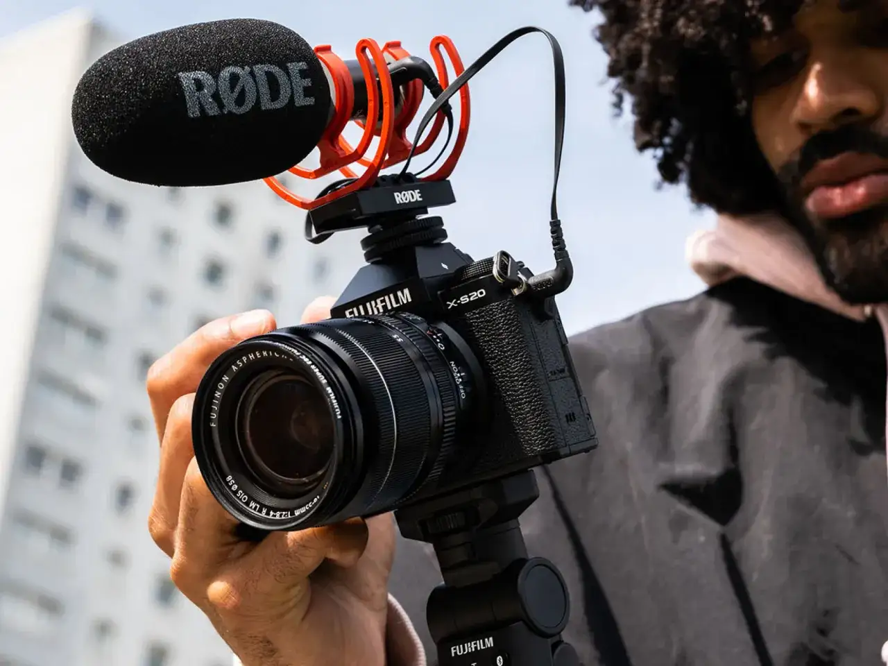 Mężczyzna trzyma aparat Fujifilm X-S20 z mikrofonem RØDE, gotowy do nagrywania.