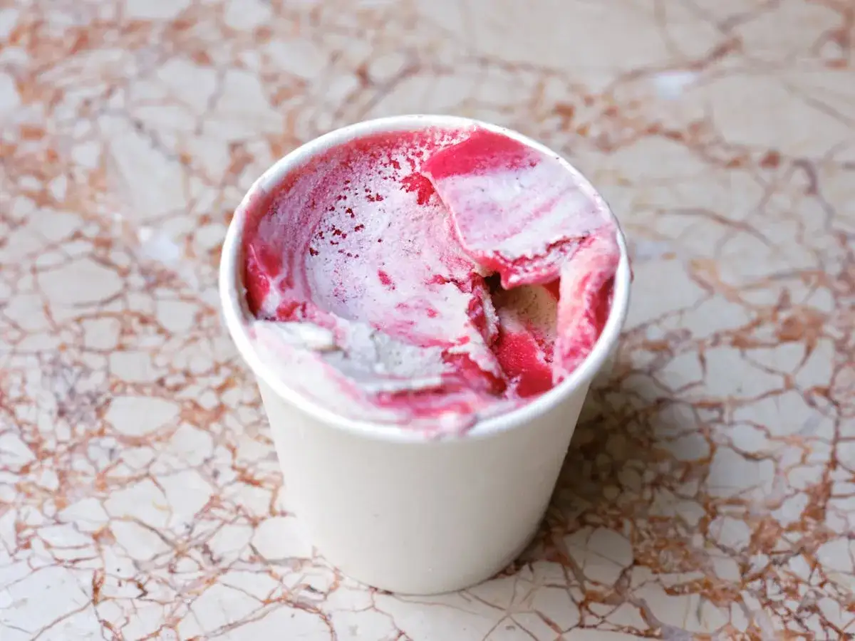 Ein Becher mit cremigem, veganem Himbeereis auf Marmor. Die rosa und weißen Schlieren versprechen süßen Genuss.