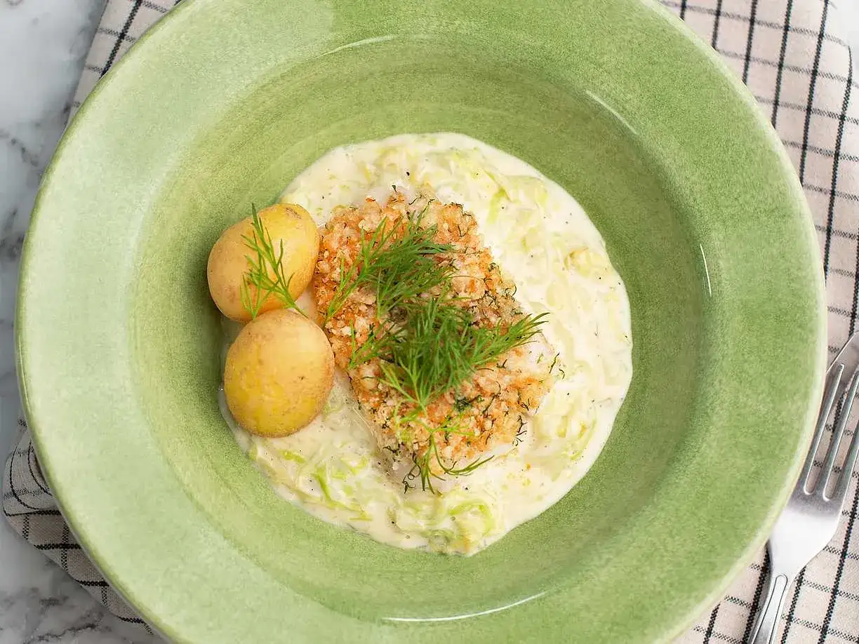 En portion stuvad spetskål med fisk, potatis och dill i en grön skål.