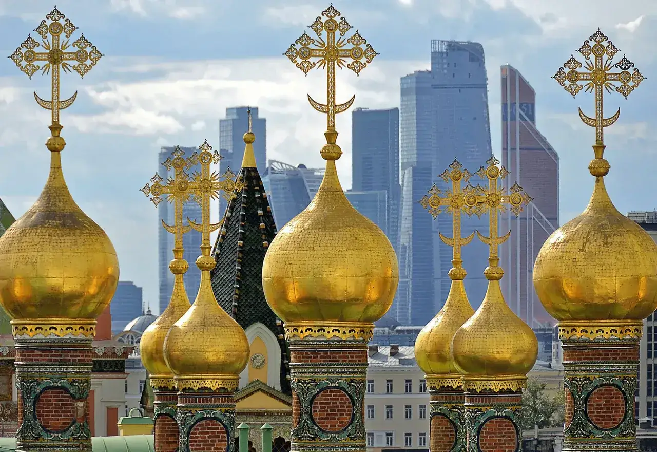 Goldene Kuppeln mit Kreuzen in Russland, im Hintergrund moderne Wolkenkratzer.
