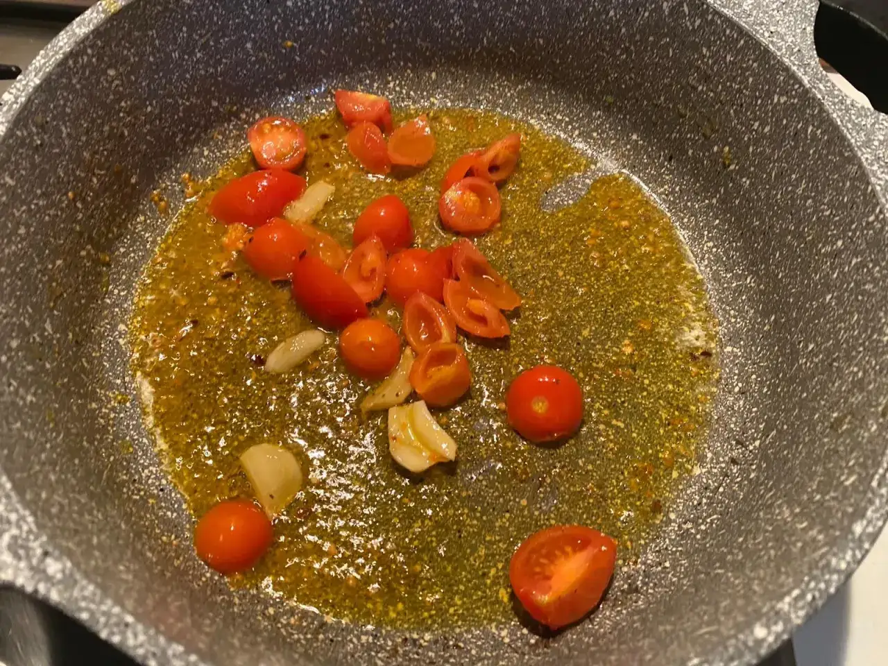Pomodorini e aglio soffriggono in padella con olio, creando un condimento saporito.