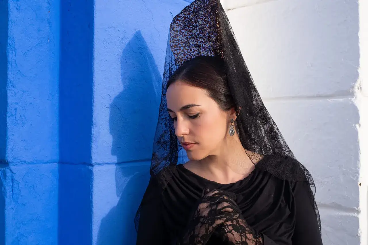 Mujer con mantilla negra, guantes de encaje y pendientes, siguiendo el protocolo para vestir de mantilla.