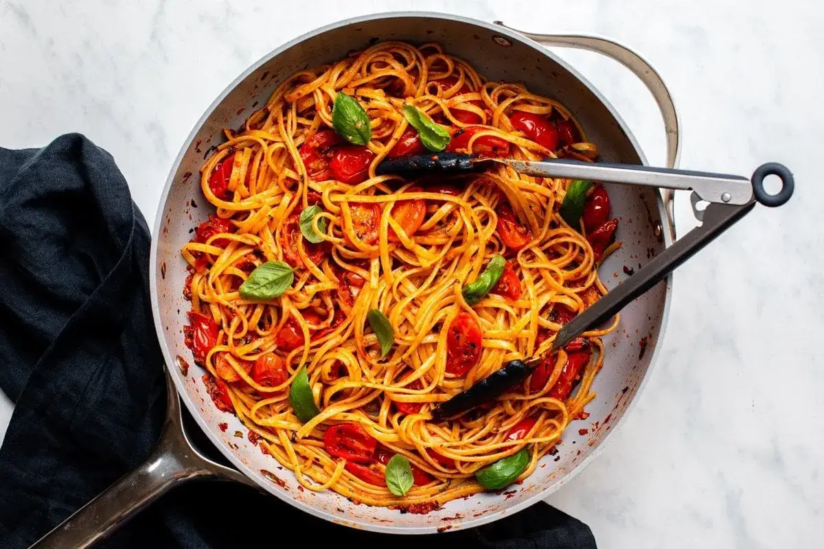 Eine Pfanne voller Penne Arrabiata, garniert mit frischem Basilikum und Kirschtomaten. Perfekt für ein feuriges Abendessen.