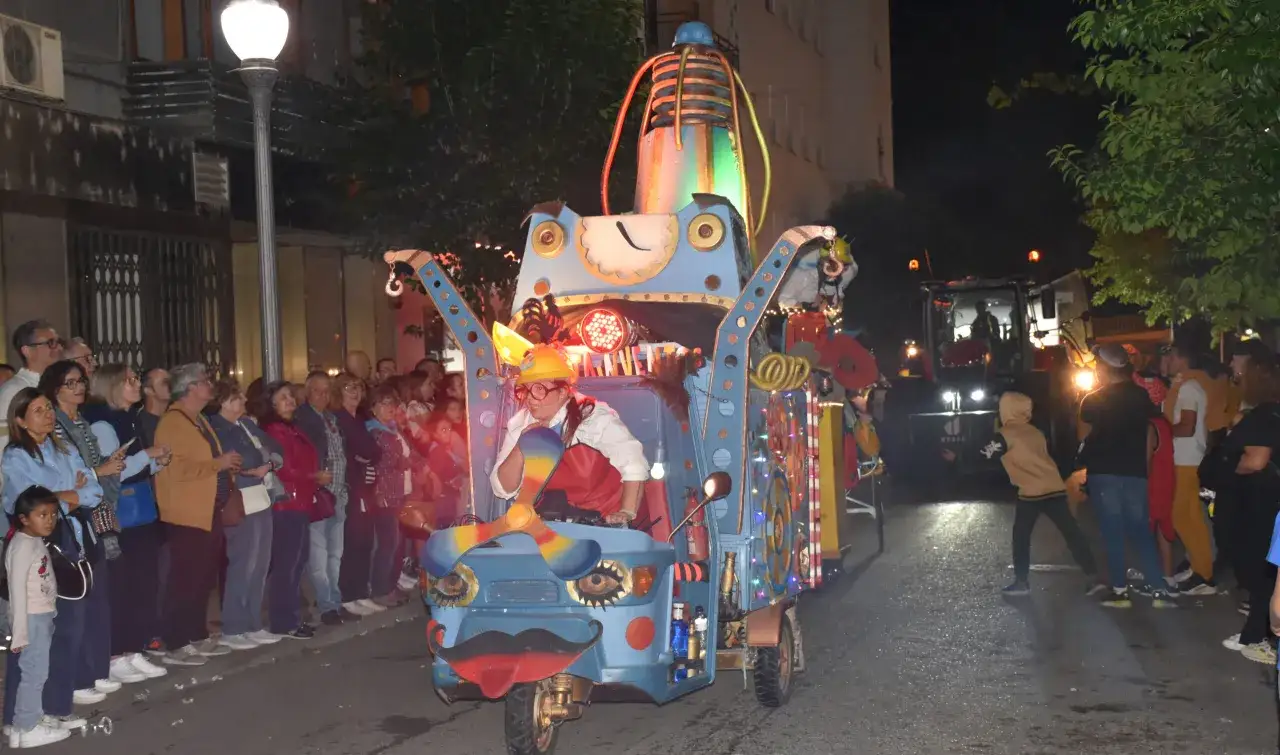 Carroza colorida y decorada con luces, con un conductor disfrazado, desfila entre la multitud durante las fiestas de Monzón.
