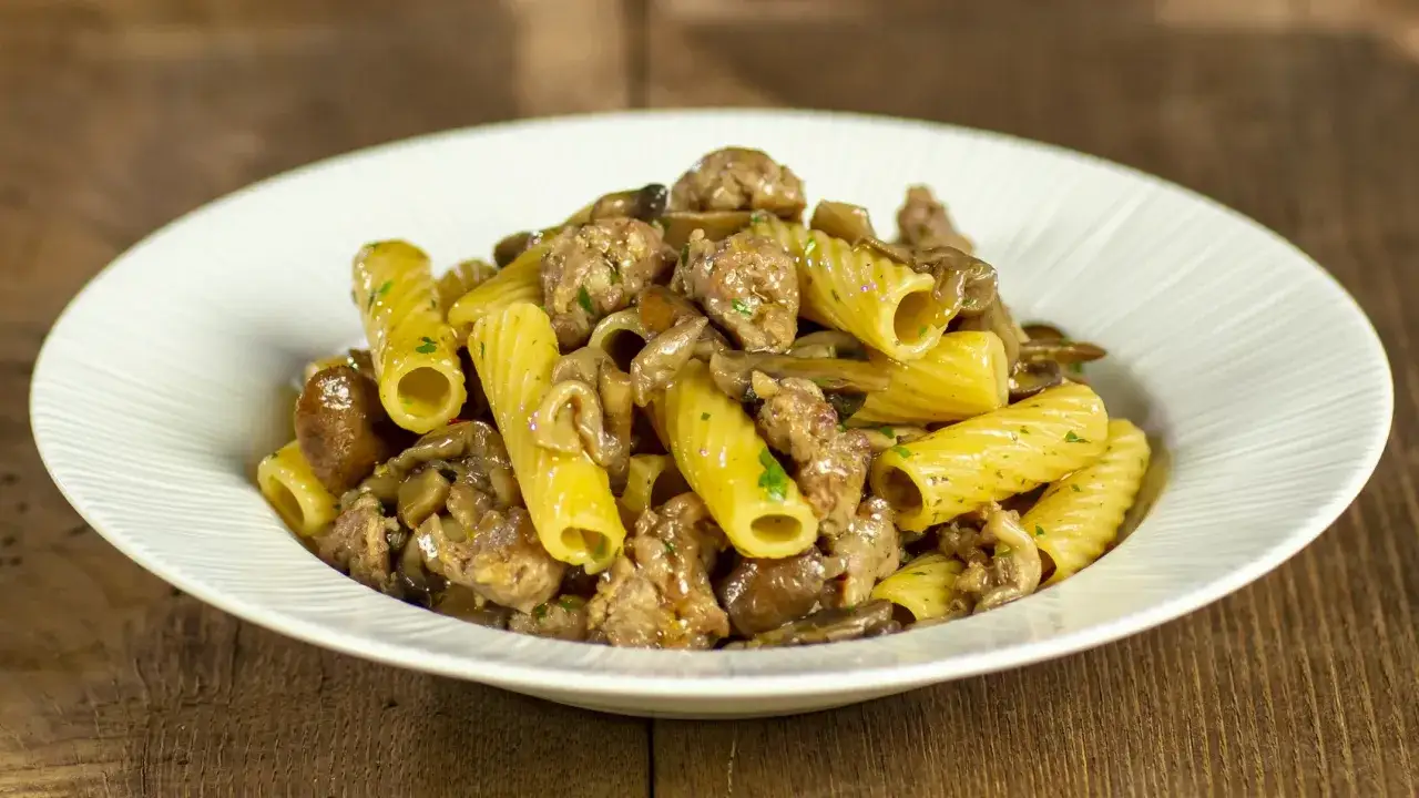 Piatto di pasta funghi e salsiccia, con rigatoni conditi con funghi trifolati e pezzetti di salsiccia saporita.