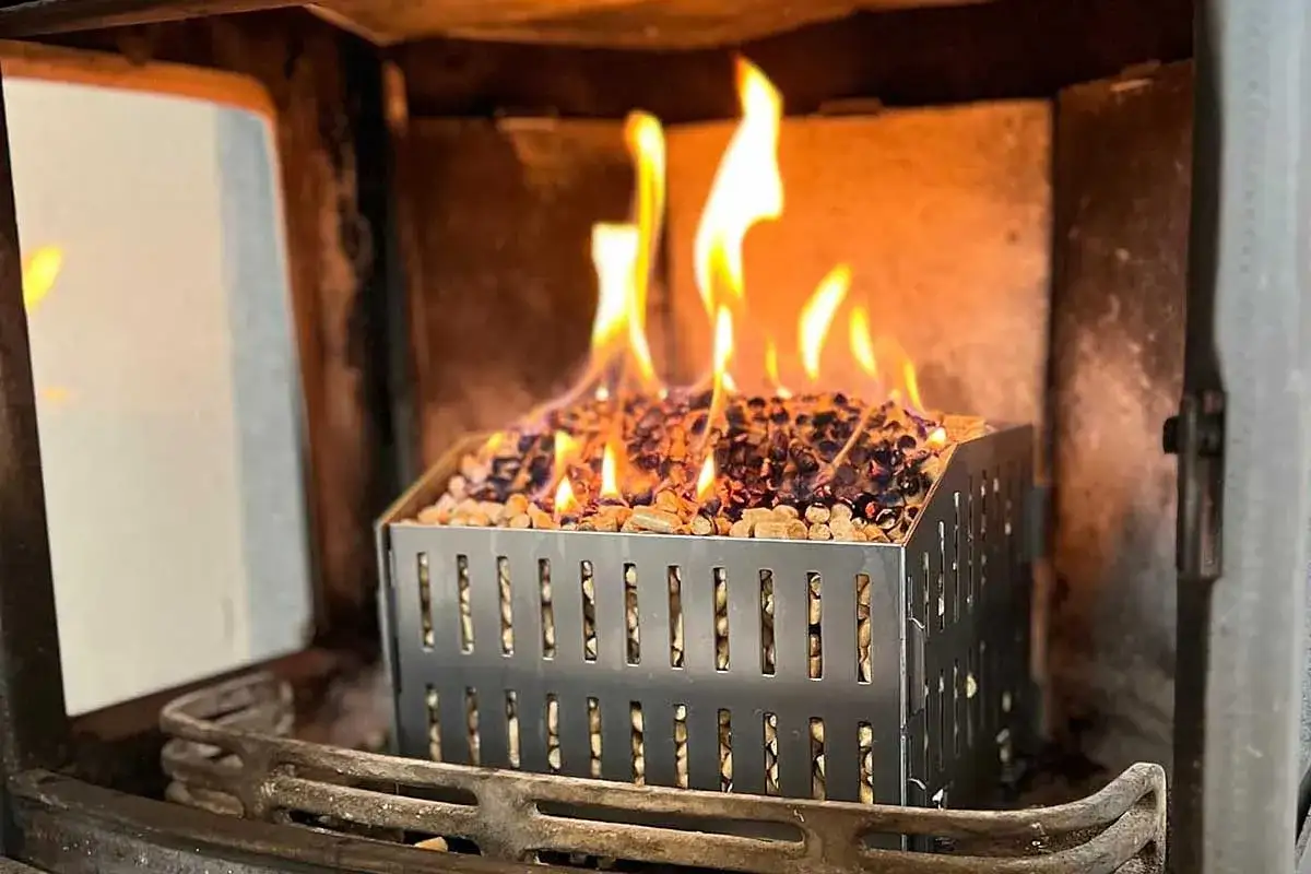 Un panier métallique rempli de pellet s'embrase dans un poêle à bois, créant une belle flamme.