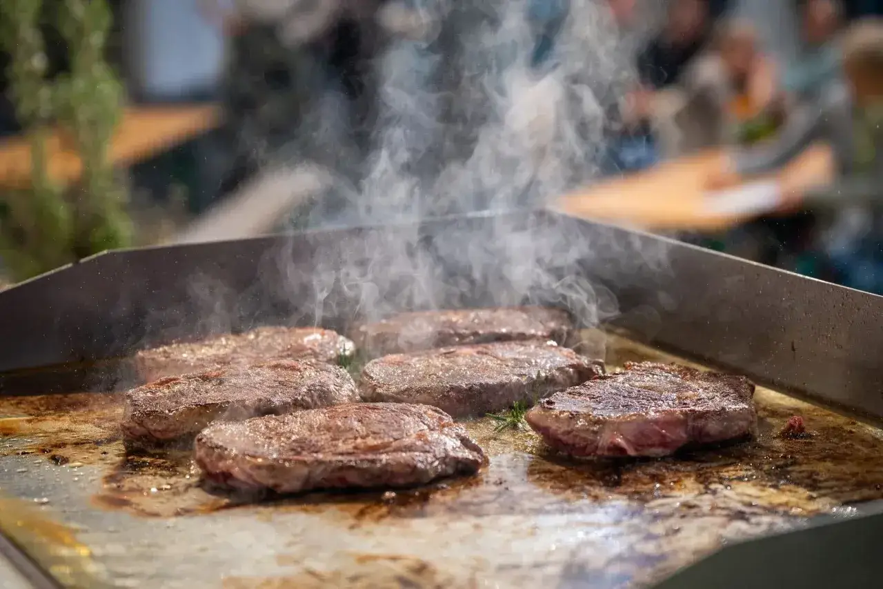 Mehrere saftige Rumpsteaks braten auf einer heißen Platte, Dampf steigt auf. Ein Fest für Fleischliebhaber!