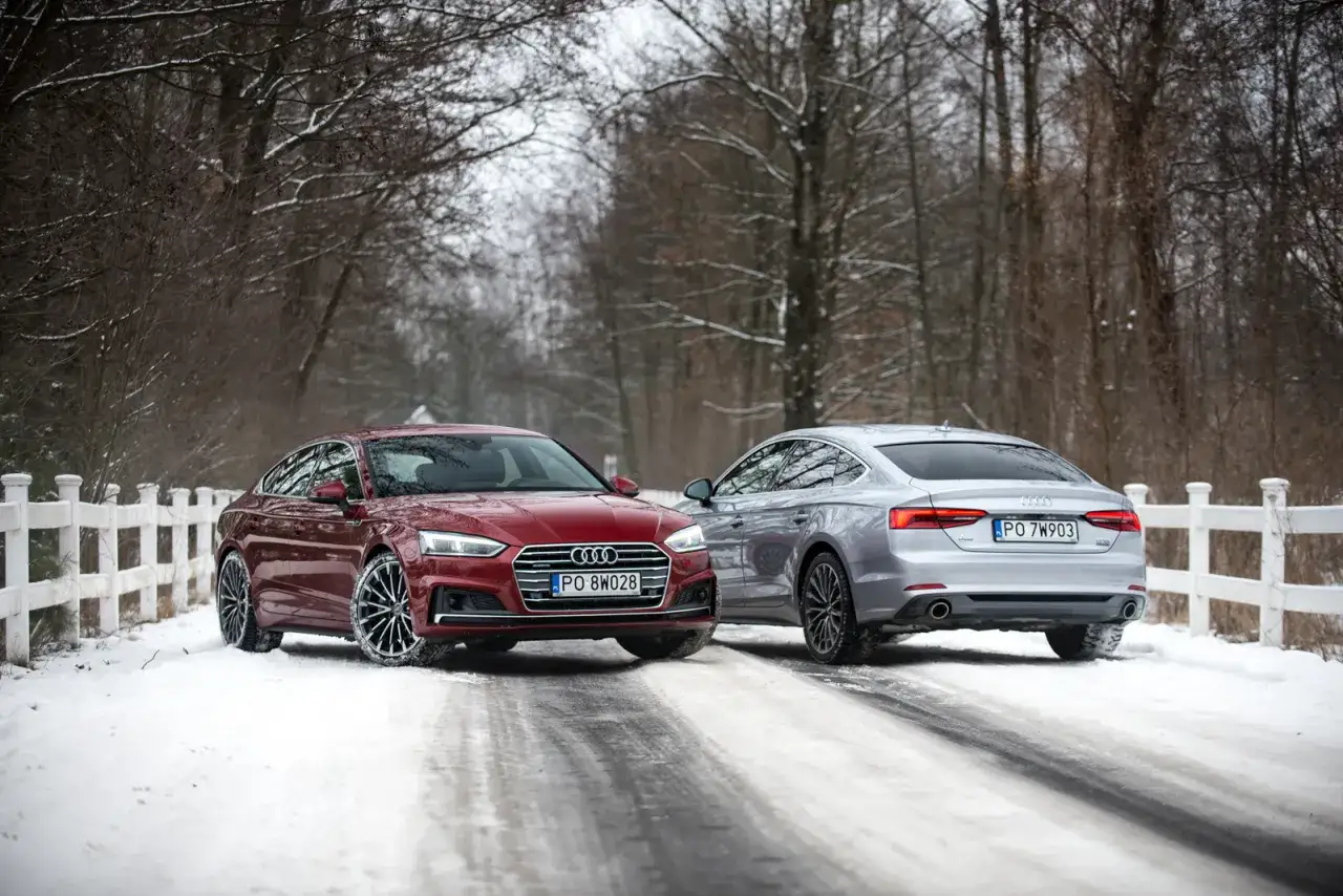 Dwa Audi Coupe, czerwone i srebrne, stoją na zaśnieżonej drodze w lesie.