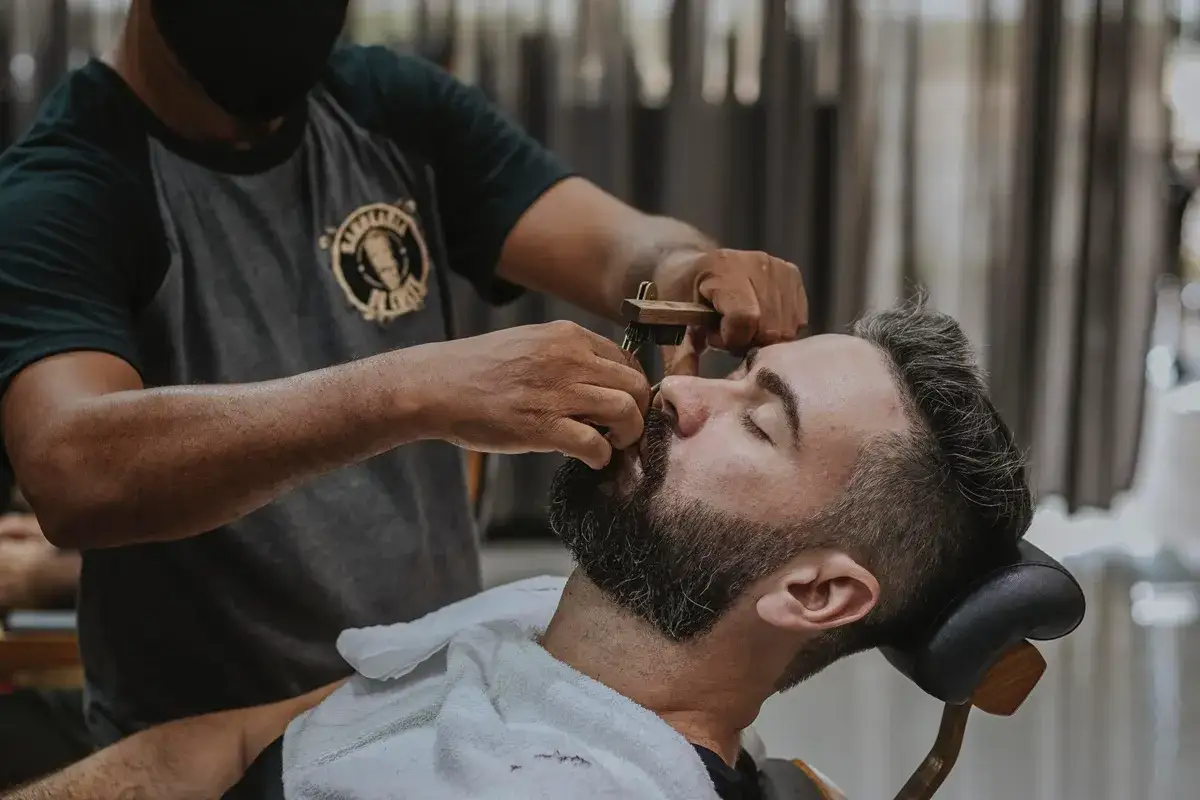 Stylista pomaga mężczyźnie jak zagęścić brodę, używając specjalnego narzędzia.