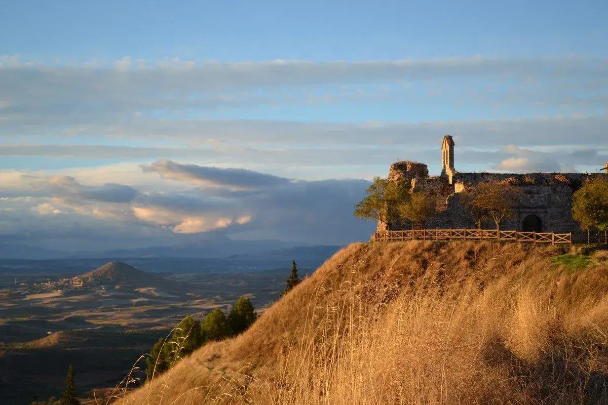 Ruinas de un castillo en un cerro, con un paisaje de la Alcarria al fondo. Un mirador natural con cielo azul y nubes.