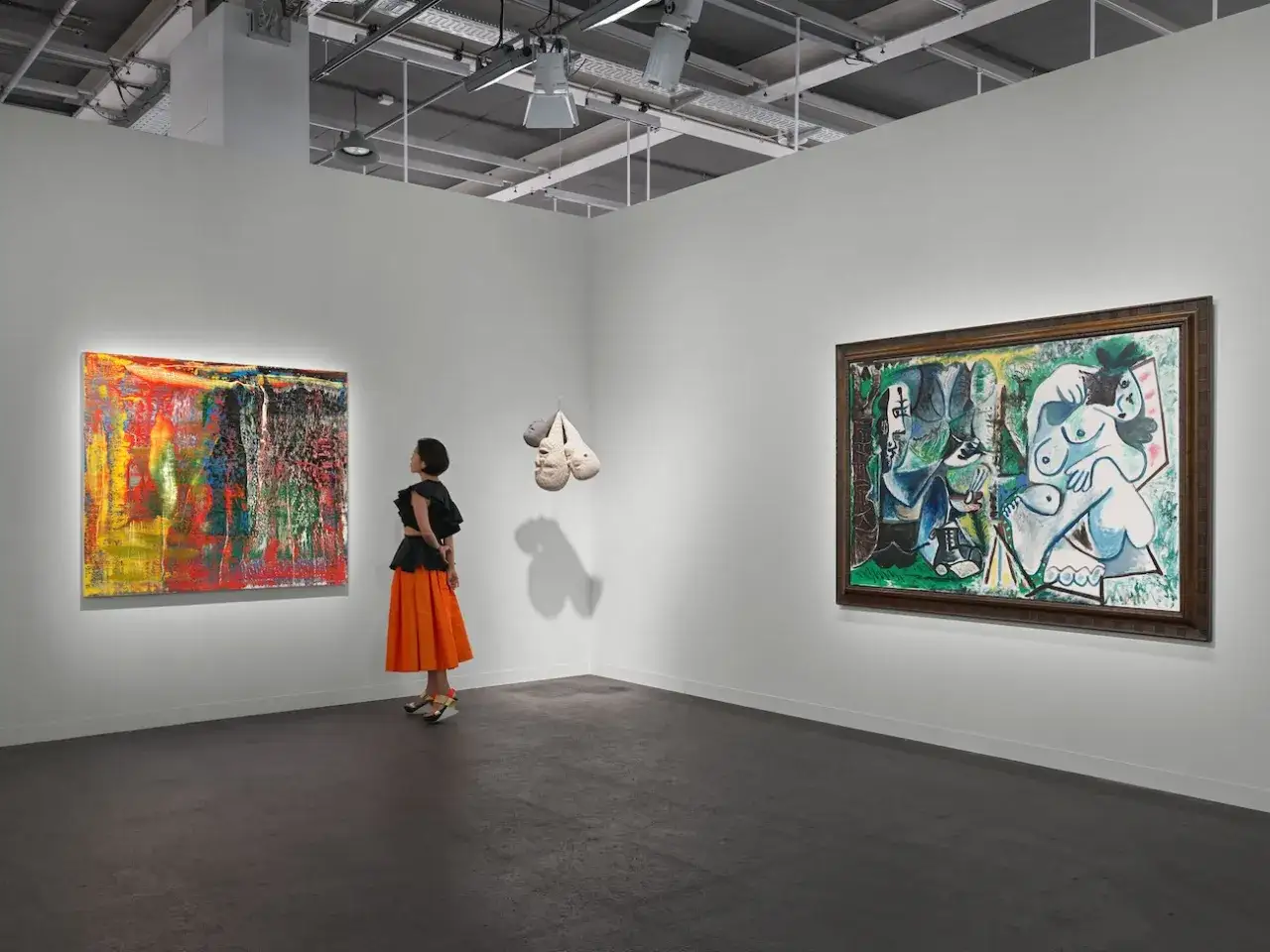 A woman in an orange skirt admires abstract art at Art Basel, a premier global art fair showcasing contemporary masterpieces.