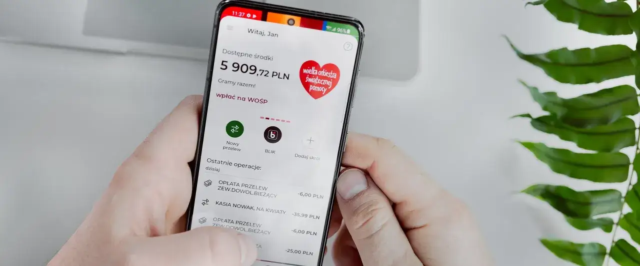Dłoń trzyma smartfon z aplikacją bankową. Na ekranie widać saldo 5909,72 PLN i opcję wpłaty na WOŚP. To idealne konto na selfie dla każdego!