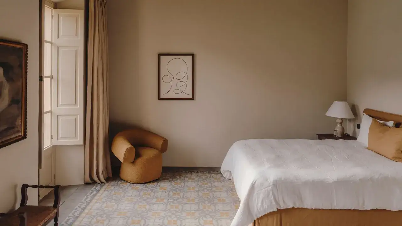 Habitaci&oacute;n con cama blanca, sill&oacute;n mostaza y suelo de baldosas. Los colores para habitaciones son c&aacute;lidos y acogedores.